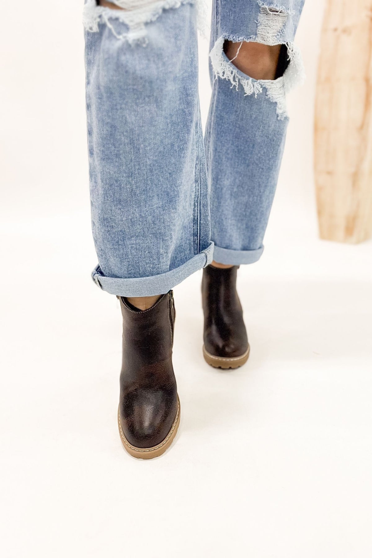 Person wearing ripped jeans and brown boots on a white background