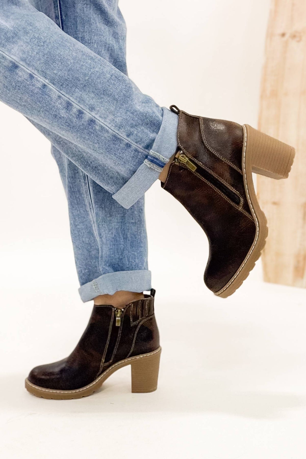 Brown ankle boots with beige soles worn with light blue jeans on a white background