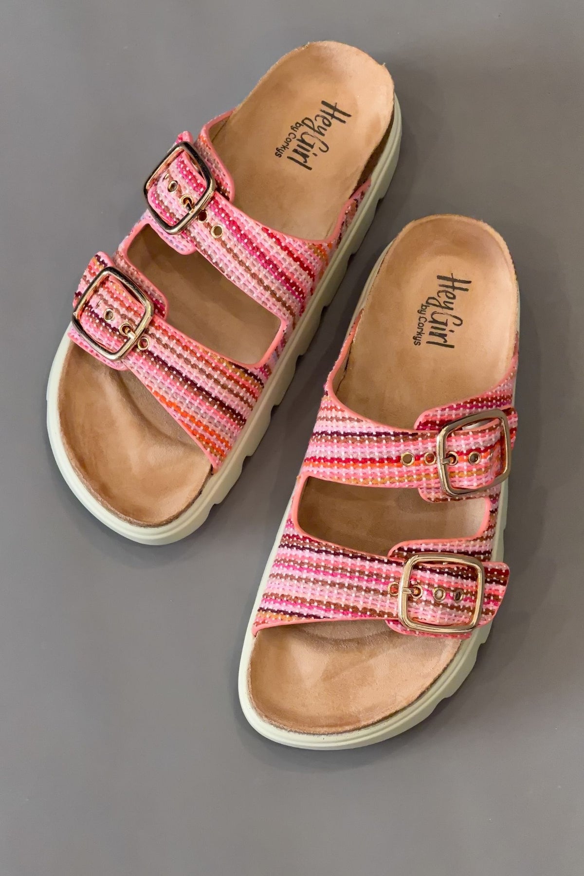 Pink sandals with brown soles on a gray background