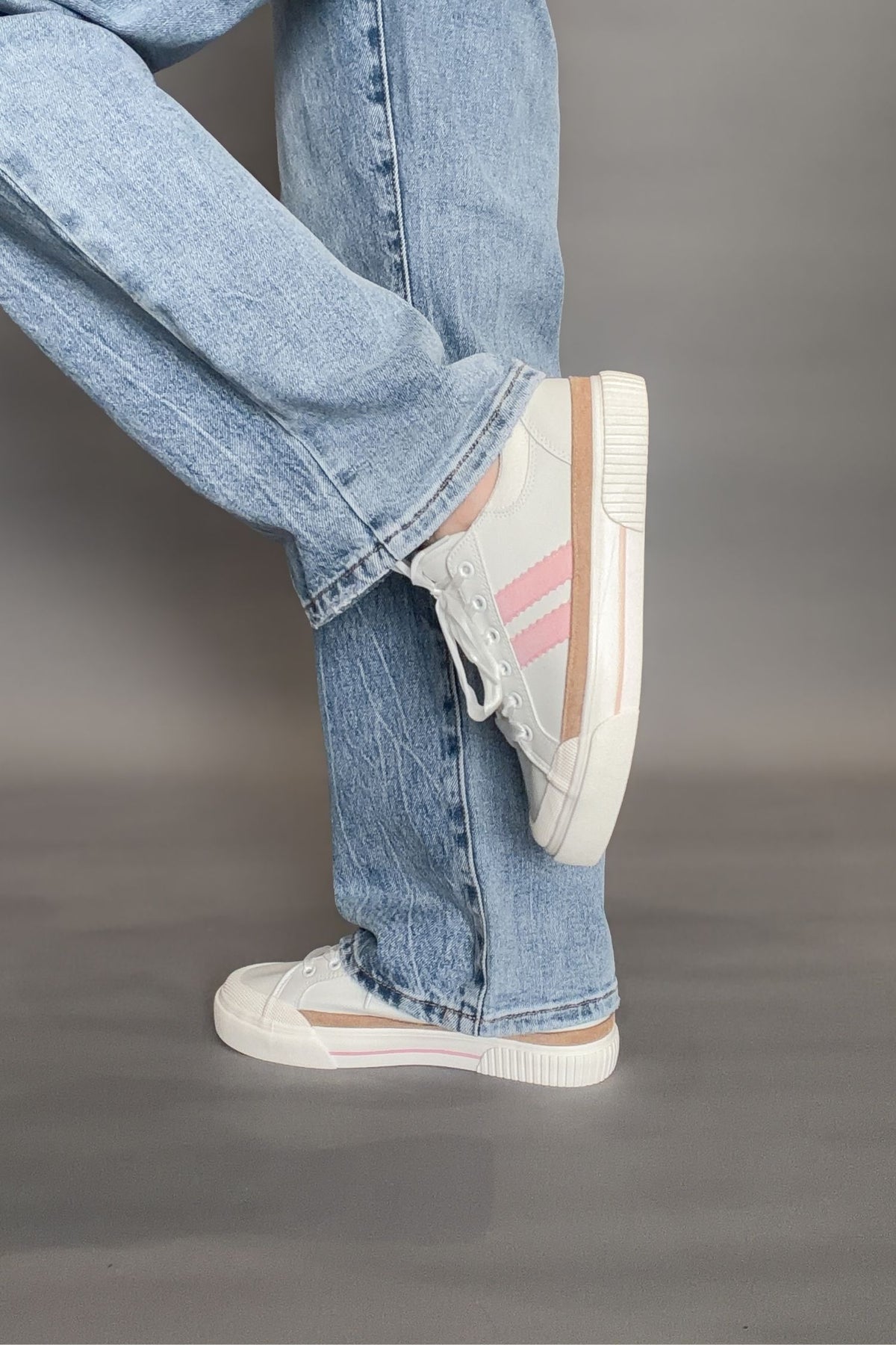 White sneakers with pink accents worn with light blue jeans on a gray background