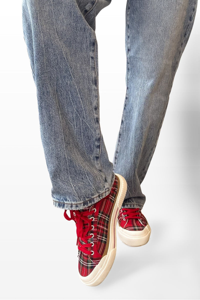 Red plaid sneakers with white soles worn with blue jeans on a light gray background