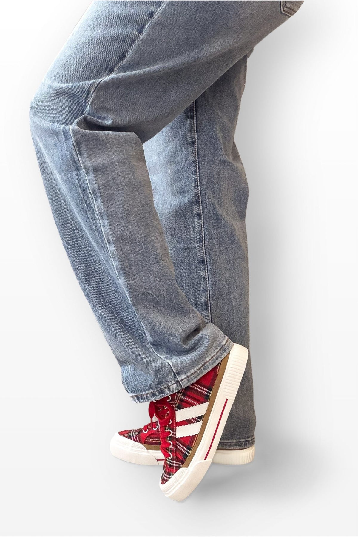 Person wearing blue jeans and red sneakers with white soles on a light gray background