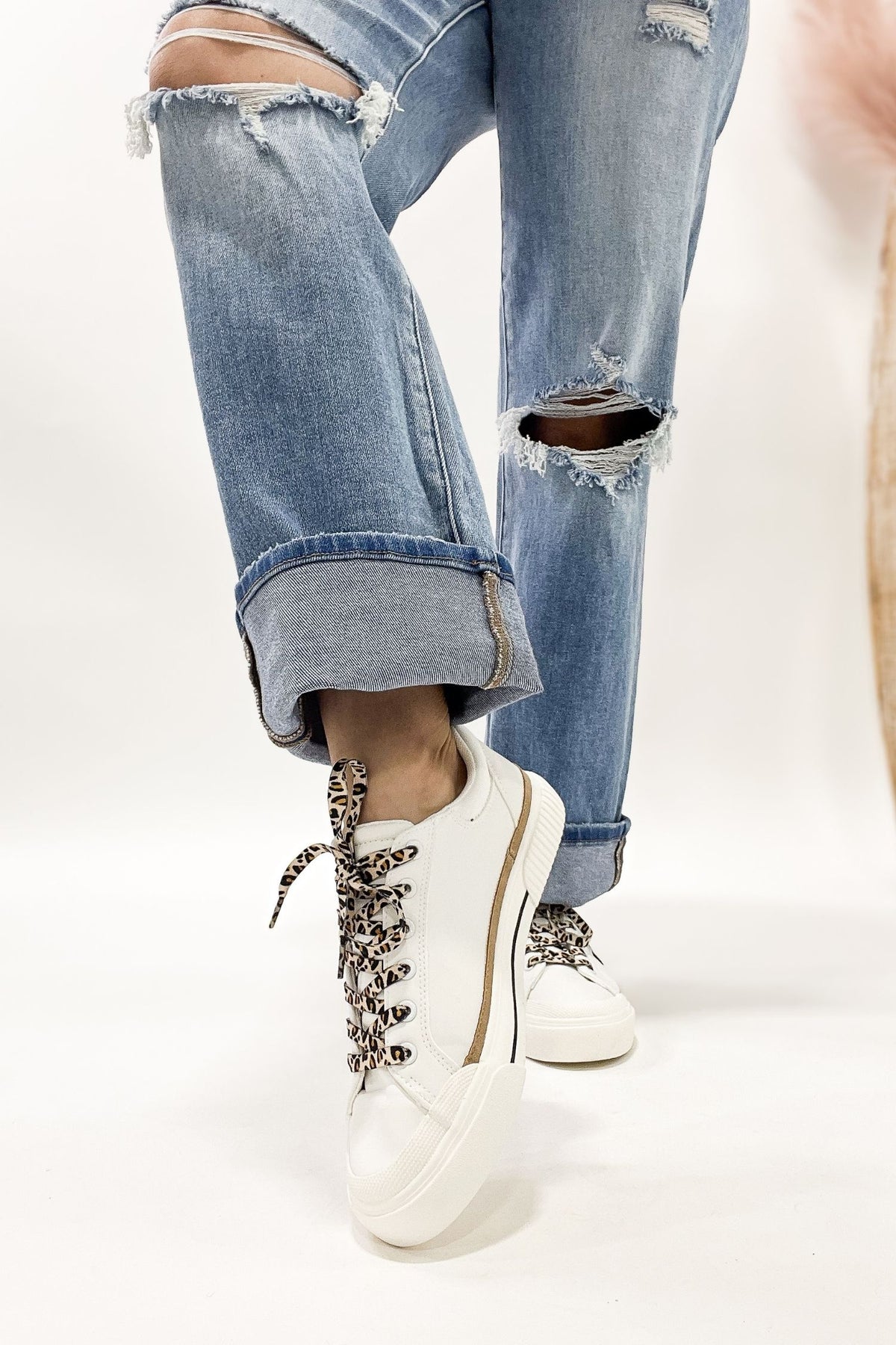 White sneakers with decorative laces worn with ripped blue jeans on a white background