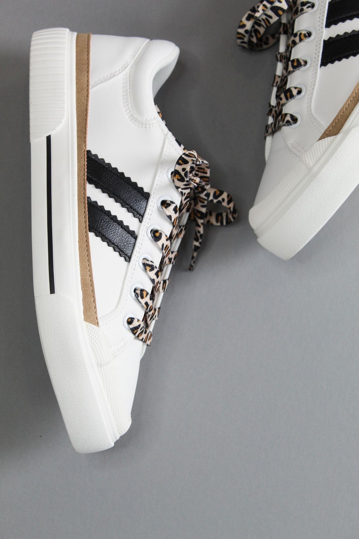 White sneakers with black stripes and leopard print laces on a gray background