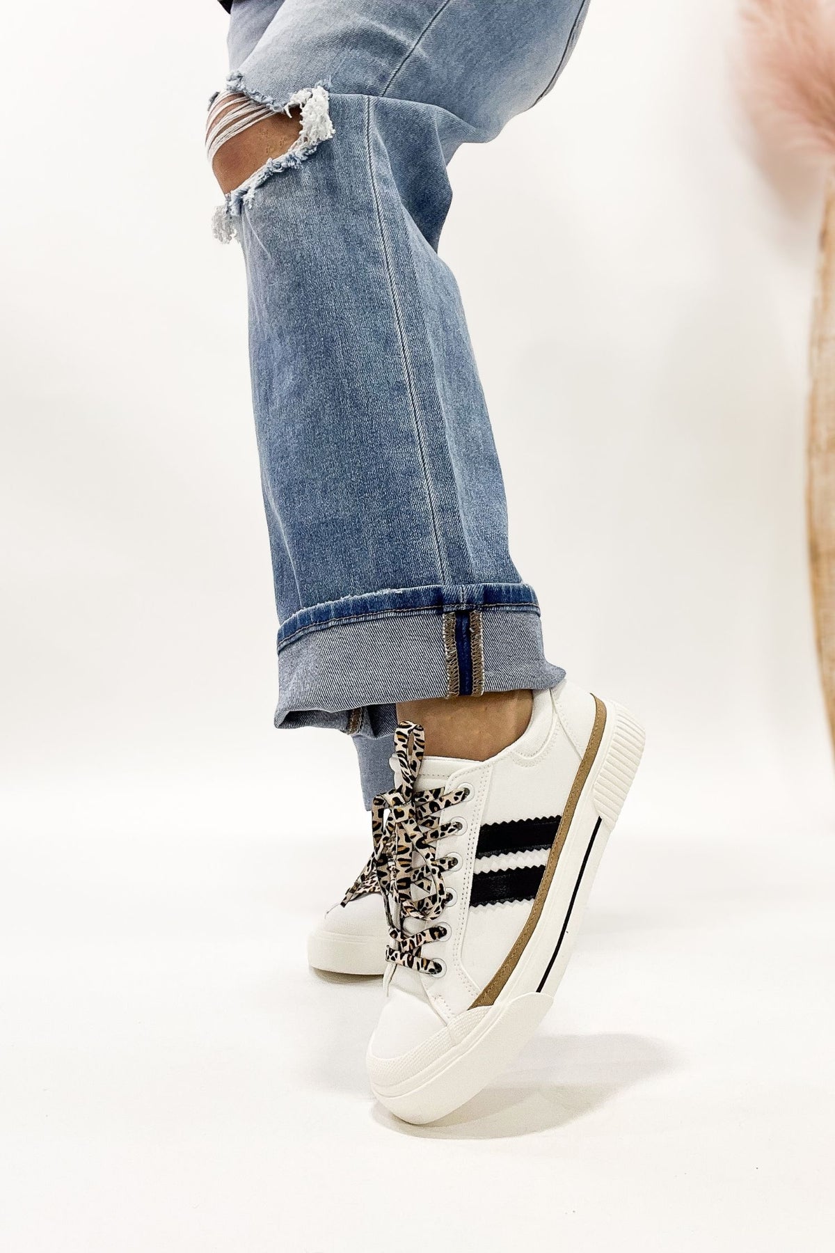 White sneakers with black and gold accents worn with rolled-up jeans on a white background
