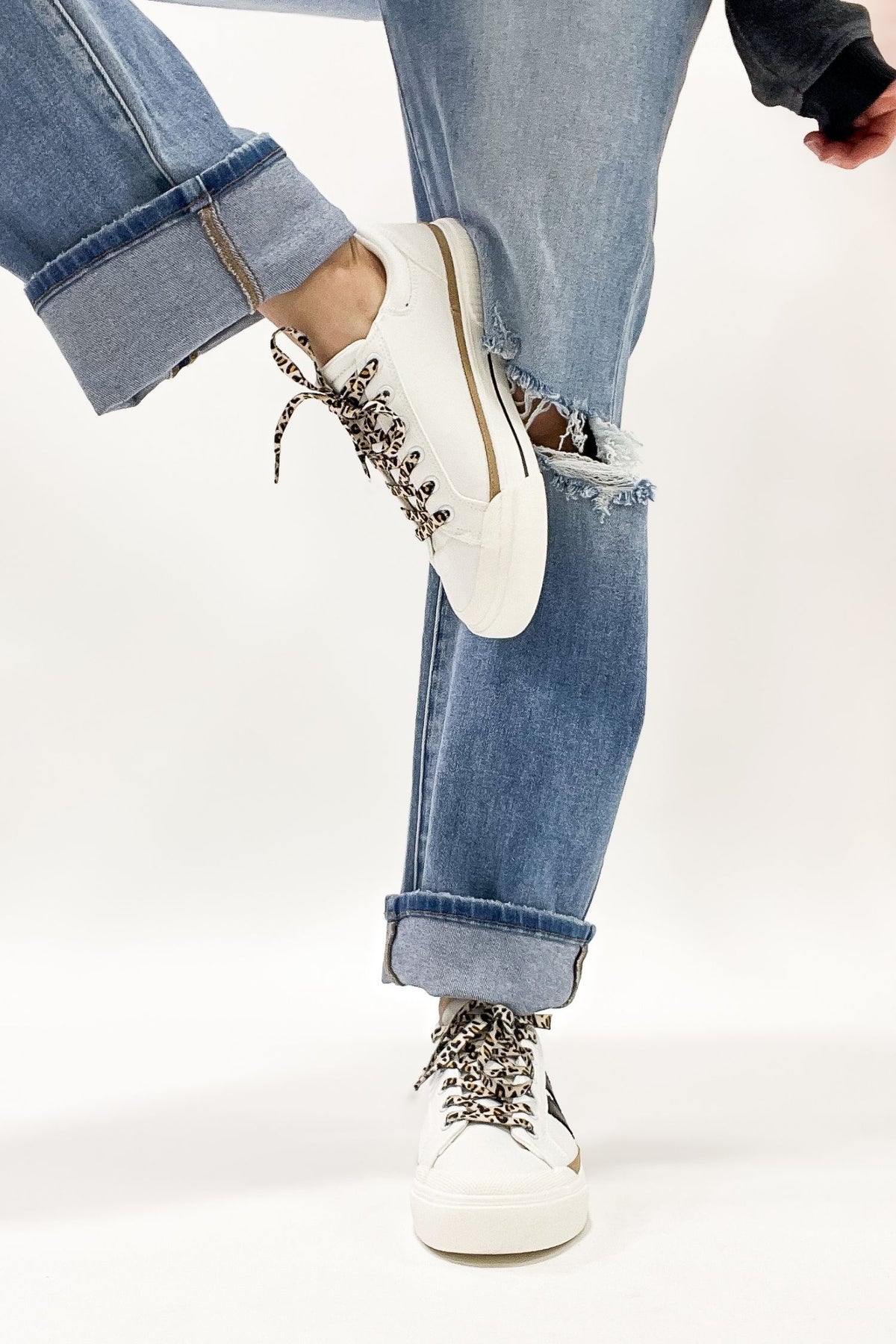 White sneakers with leopard laces worn with rolled-up blue jeans on a white background