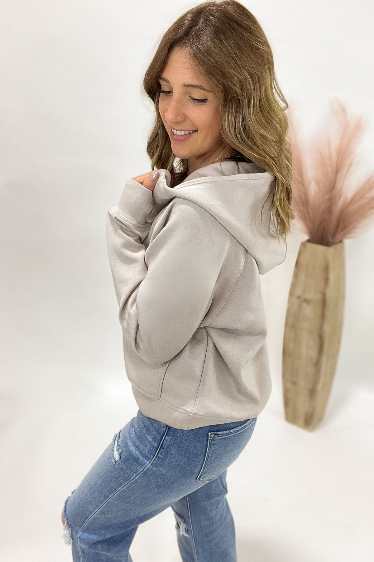 woman wearing a cream half zip and jeans standing in front of a white background