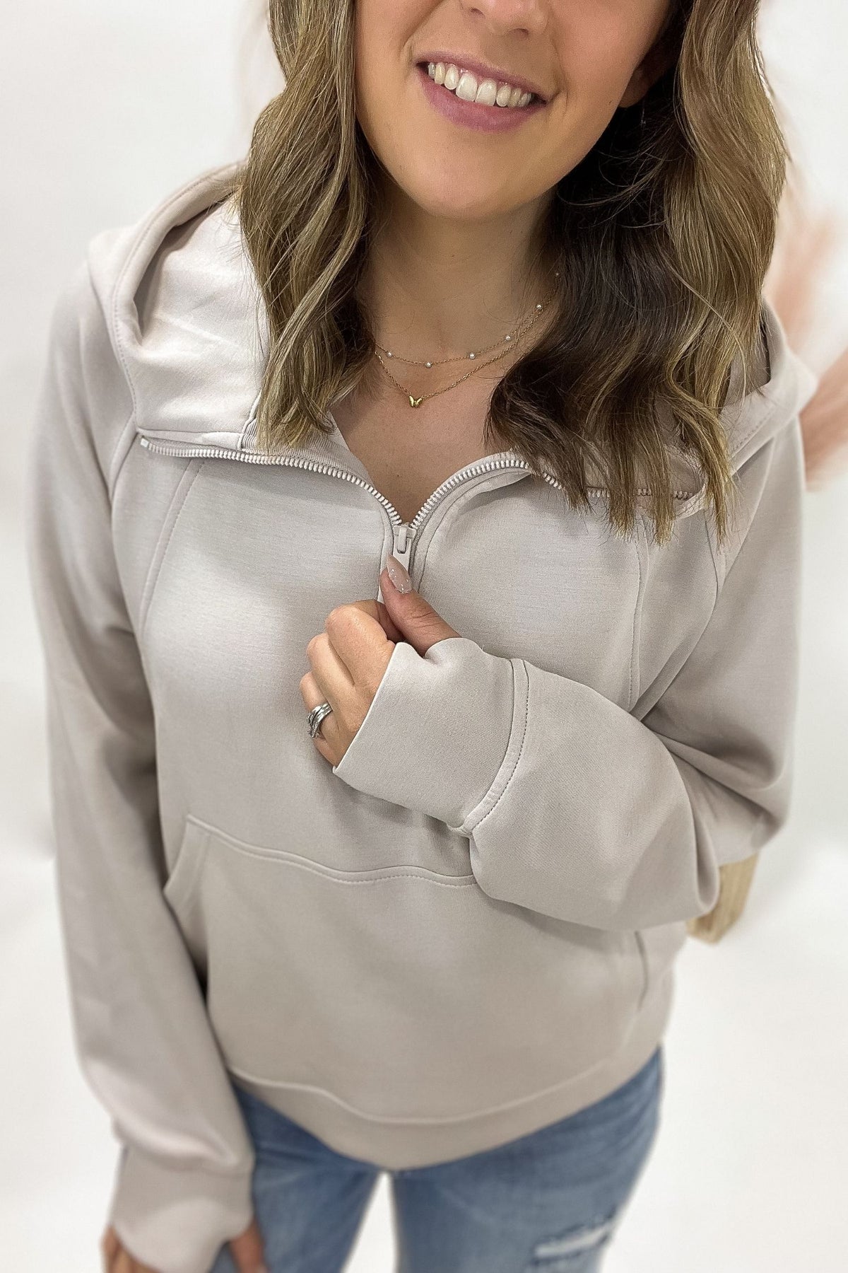 woman wearing a cream half zip standing in front of a white background