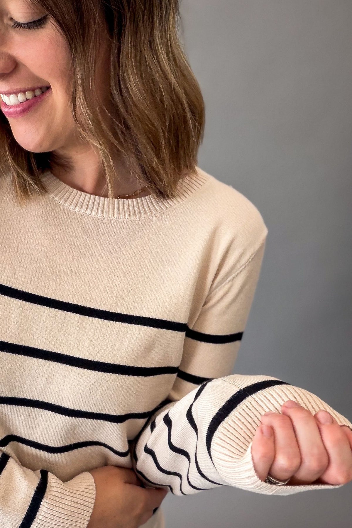A woman wearing a cream-colored knit sweater with horizontal black stripes, shown from the chest up against a plain gray background.