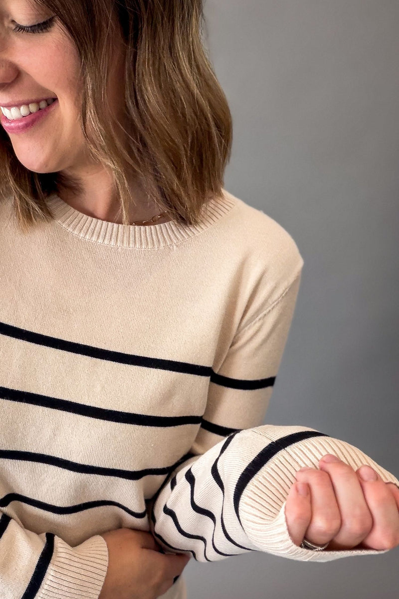 A woman wearing a cream-colored knit sweater with horizontal black stripes, shown from the chest up against a plain gray background.