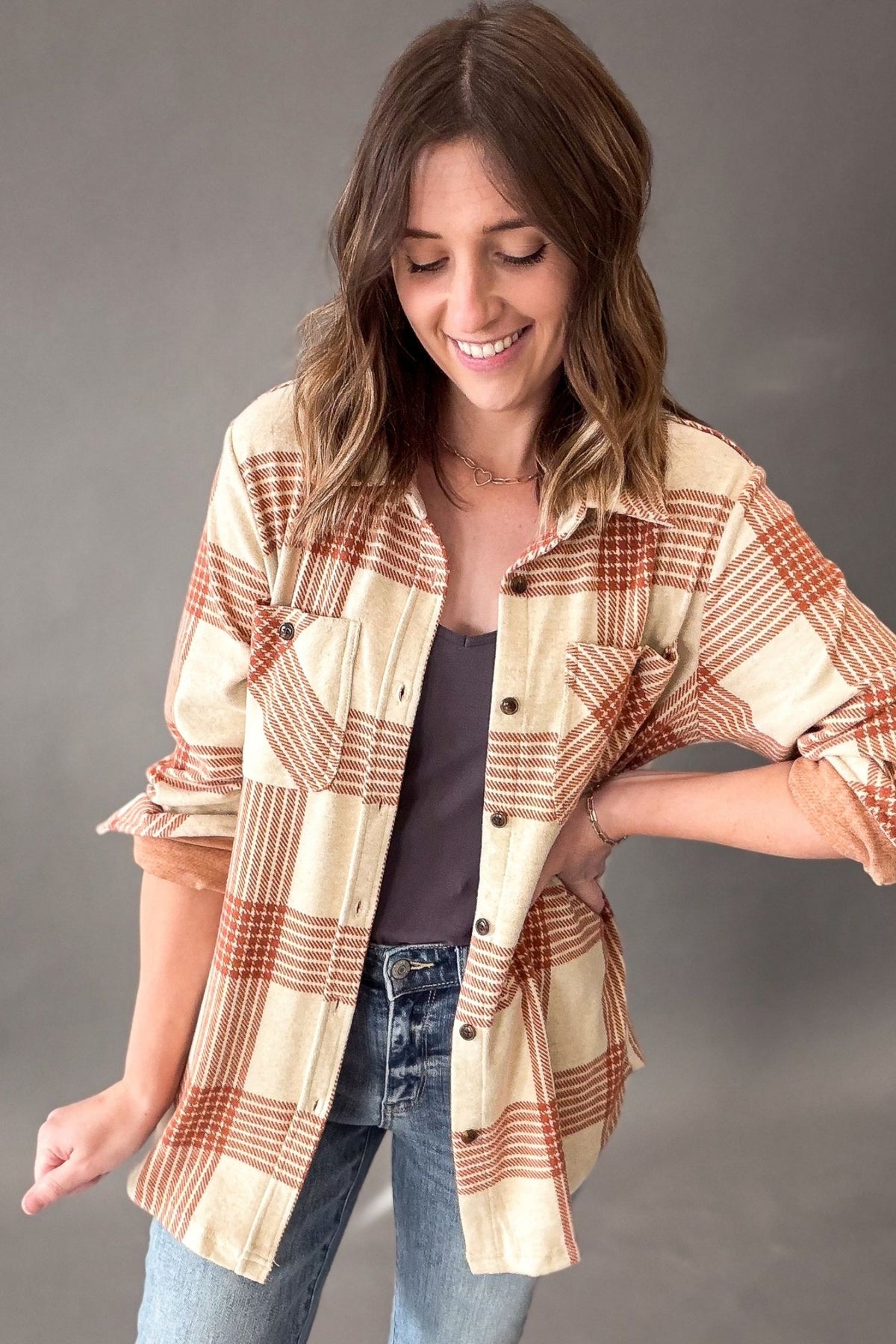 woman wearing a cream and rust plaid button up with a charcoal tank and medium wash denim on a grey studio backdrop