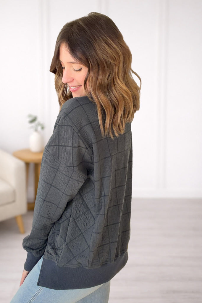 Woman wearing a gray quilted jacket in a room with a white wall and a small table.