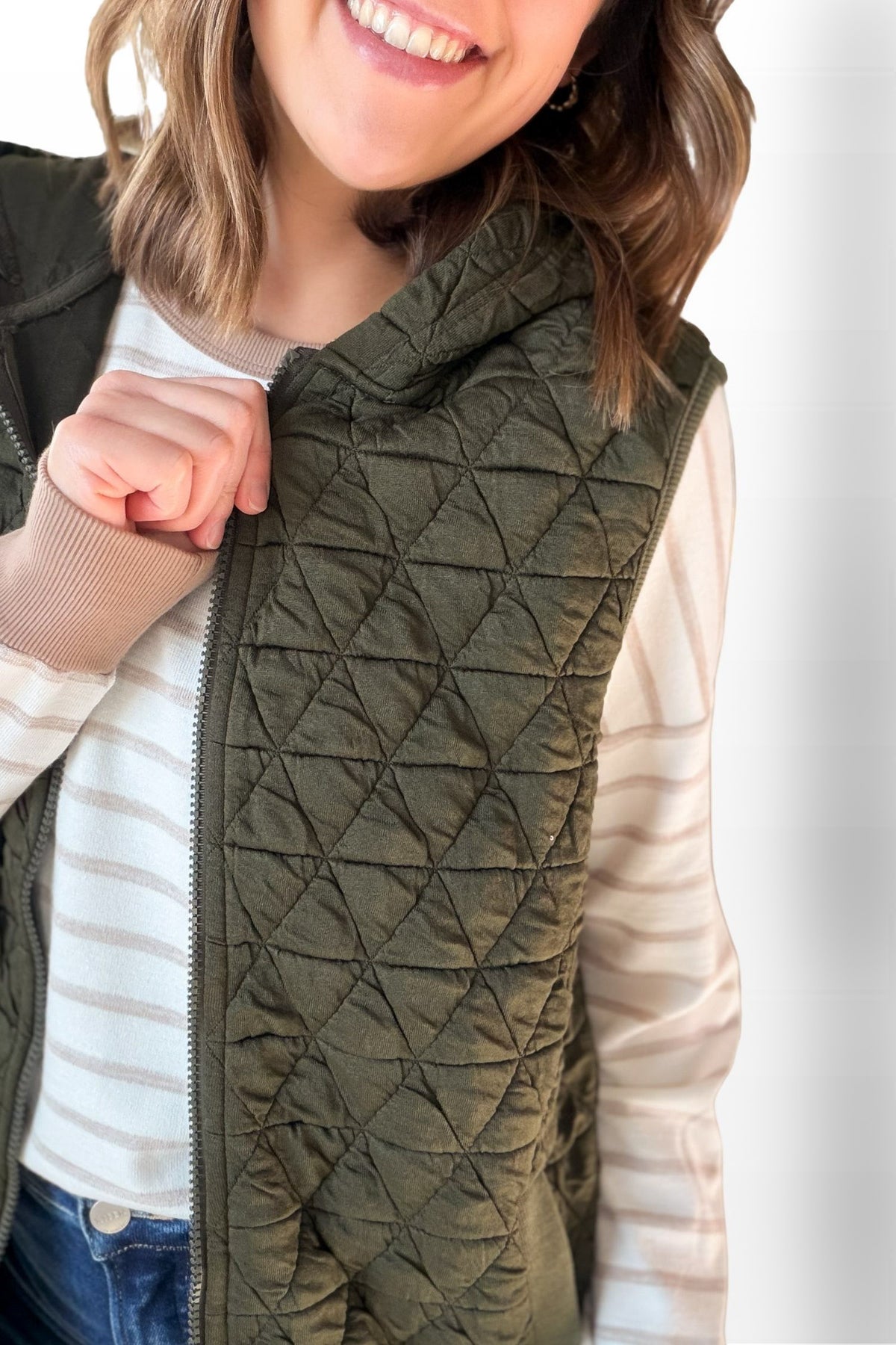 Person wearing a green quilted vest with a plain background