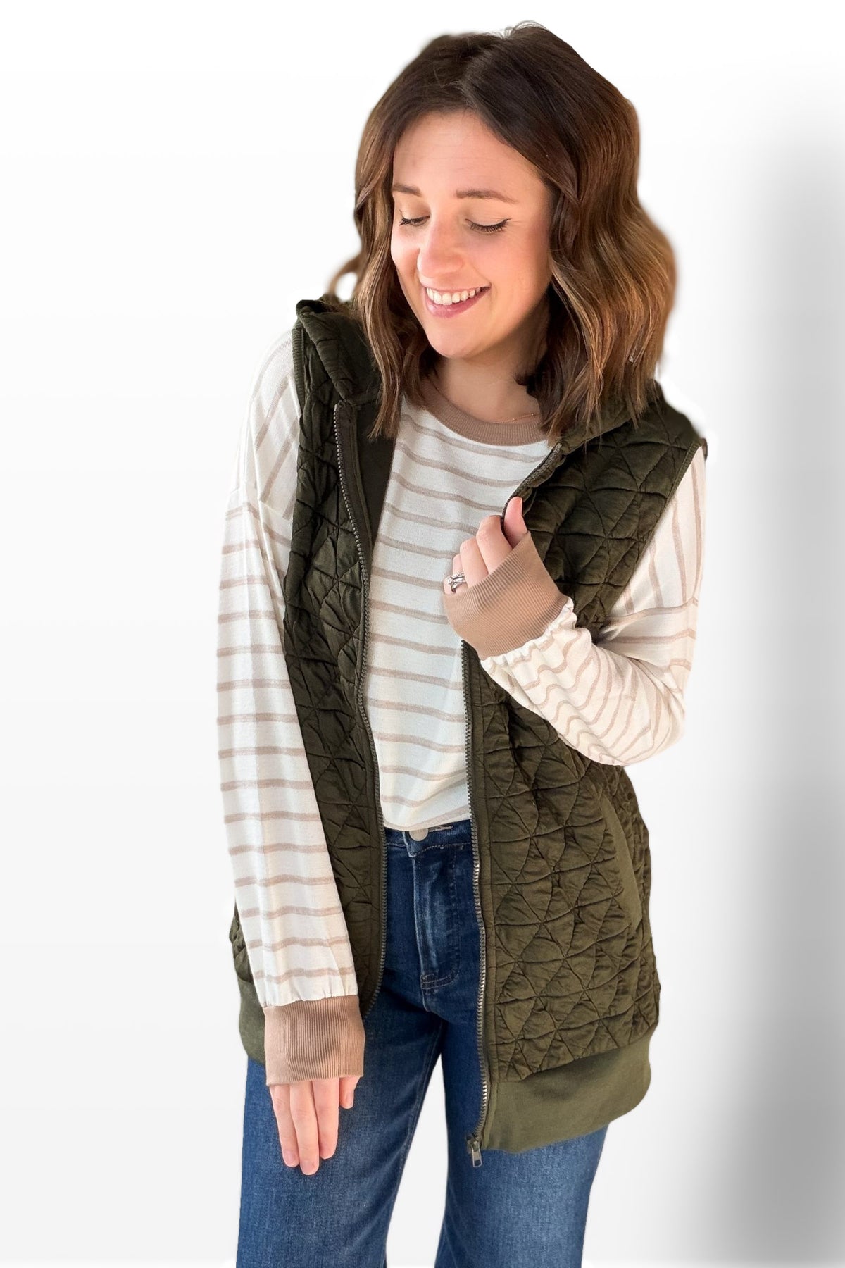 Woman wearing a green quilted vest over a striped shirt on a white background