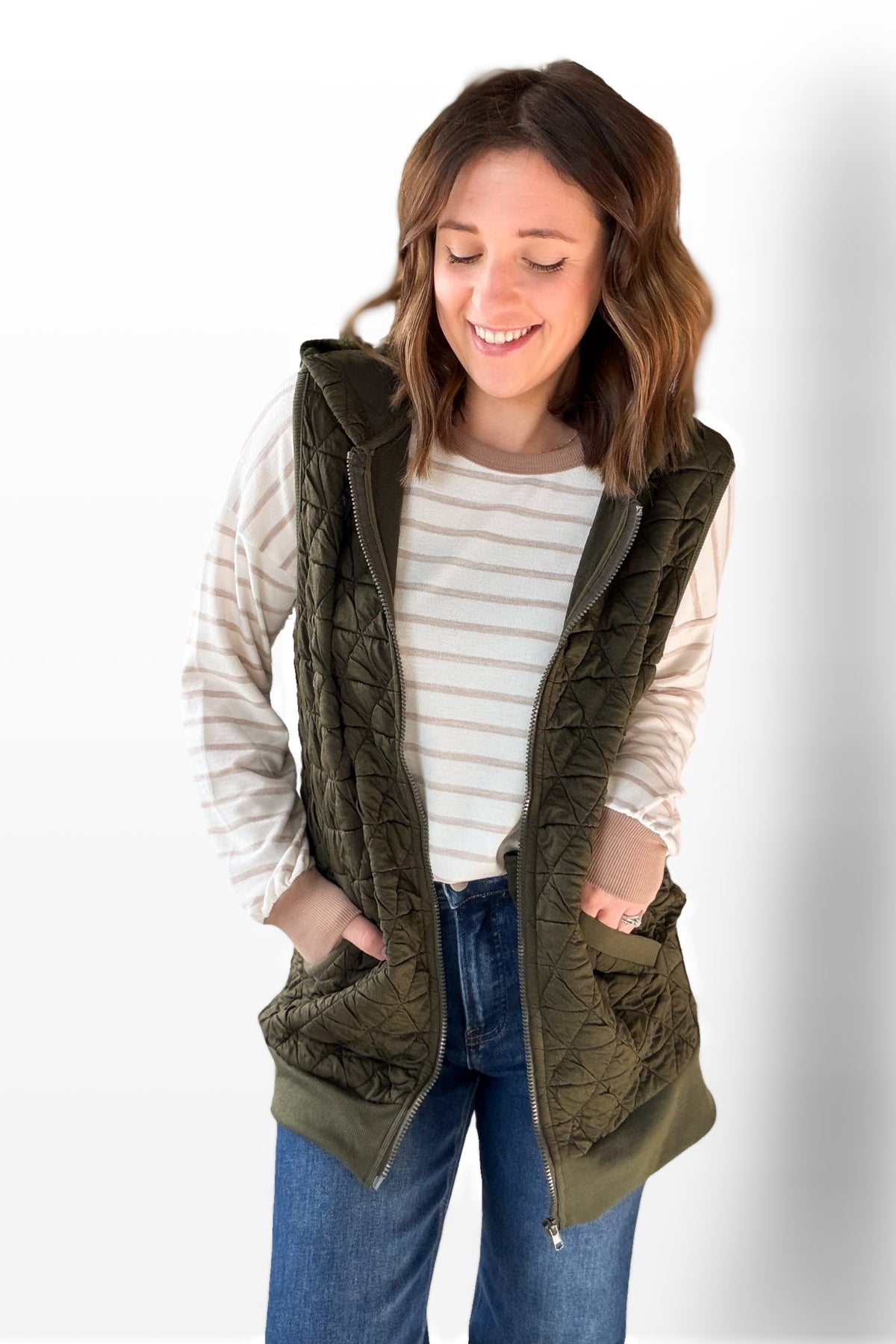 Woman wearing an olive green vest over a striped shirt with a white background