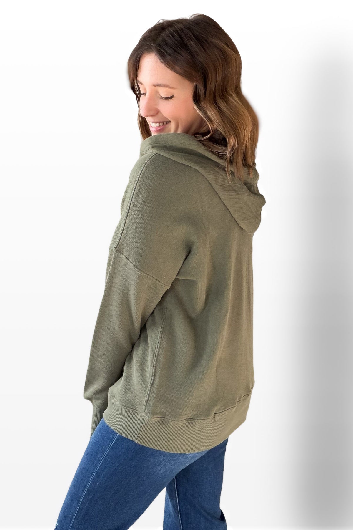 Woman wearing an olive green hoodie and blue jeans on a white background