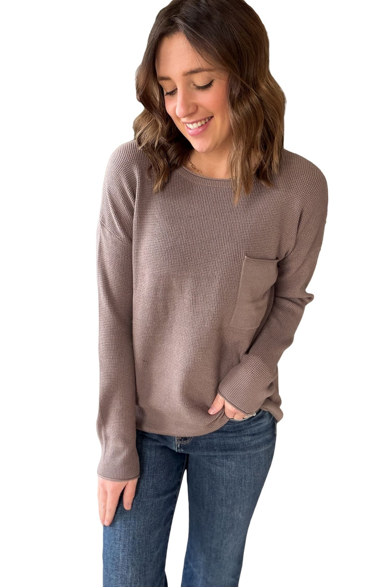 Woman wearing a brown sweater and blue jeans on a white background