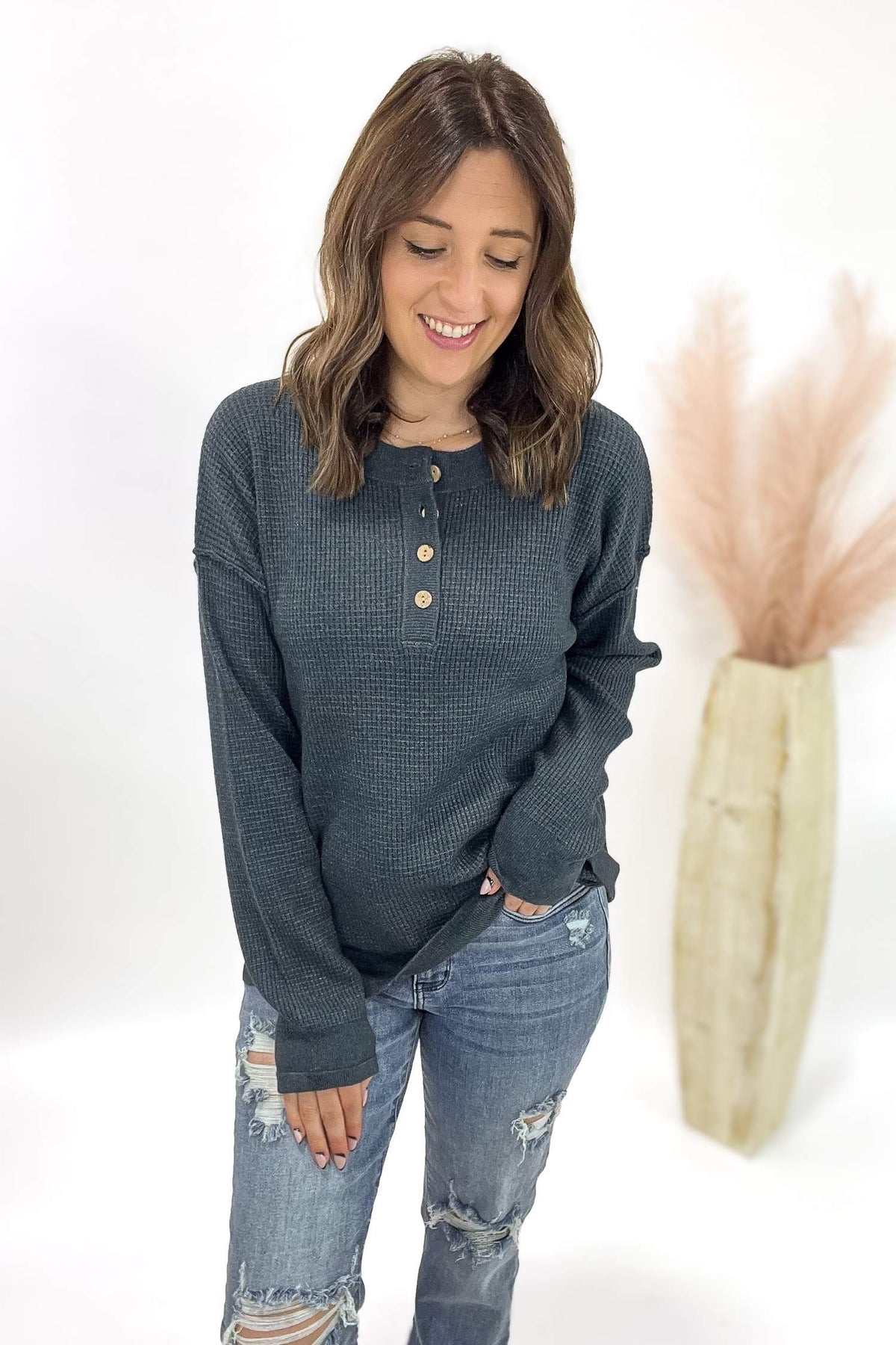 Woman wearing a dark blue long-sleeve shirt with button details and ripped jeans, standing against a white background.