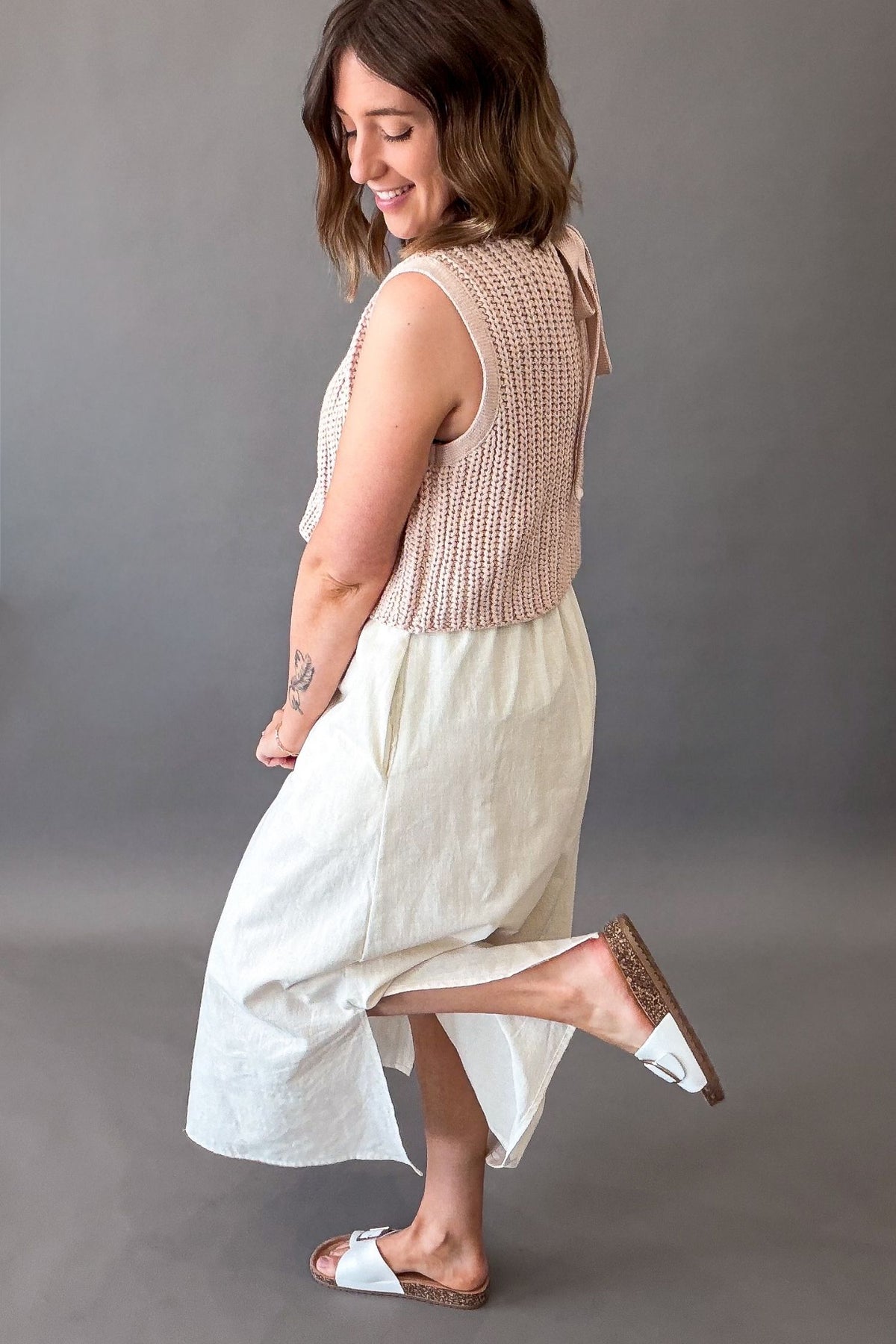 Woman wearing a dusty blush chunky sweater twofer midi dress with layered knit top and flowy lined skirt showing the side details (pockets, side slit and coverage)