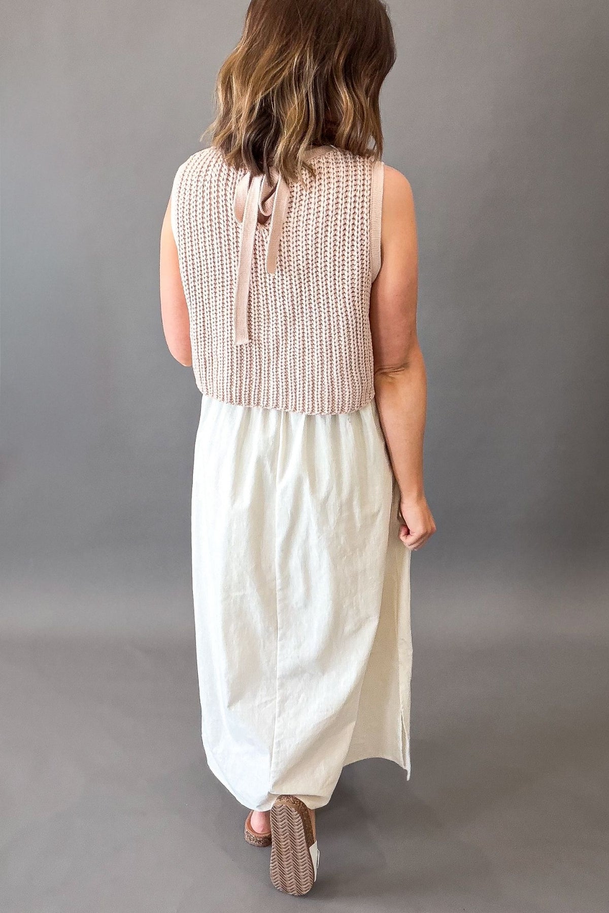 Woman wearing a dusty blush chunky sweater twofer midi dress with layered knit top and flowy lined skirt with side slits showing full back details