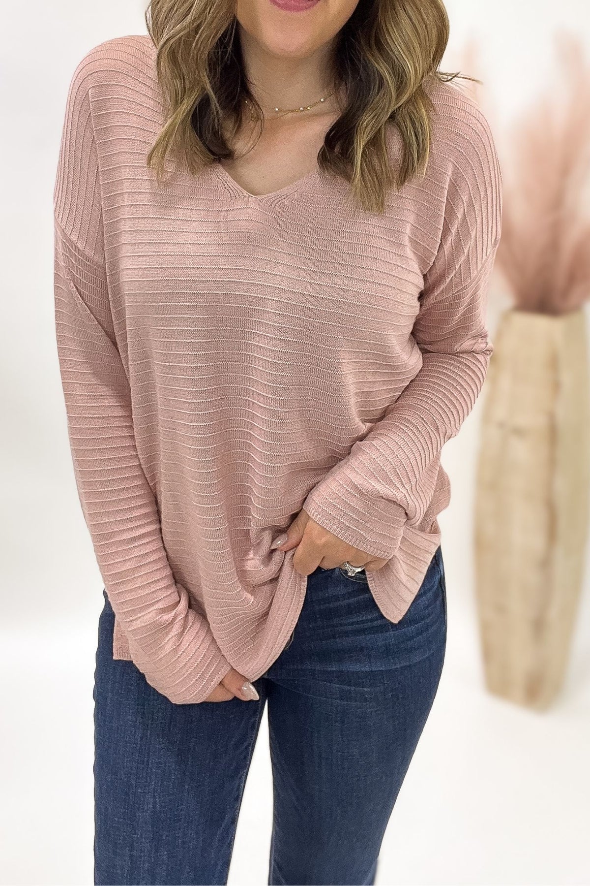 Person wearing a pink ribbed sweater and blue jeans on a white background