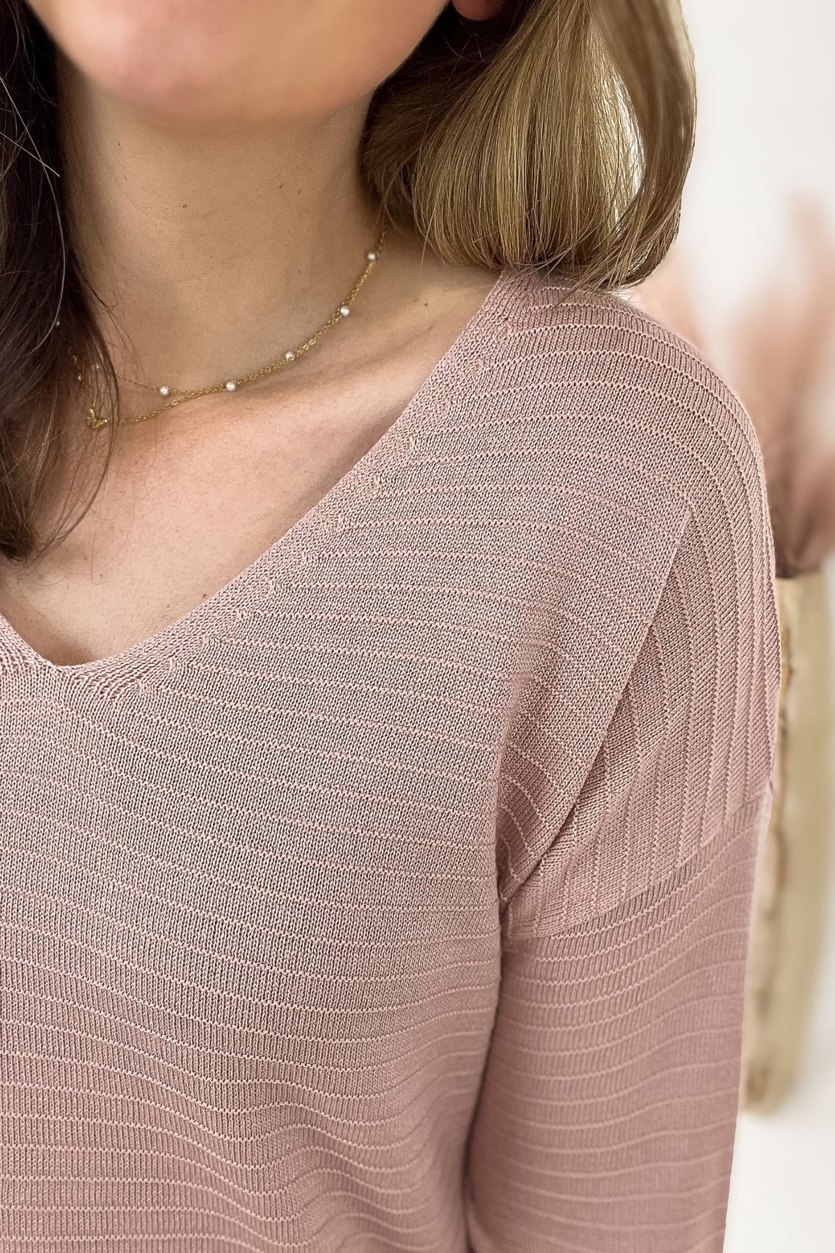Close-up of a person wearing a pink textured top with a blurred background