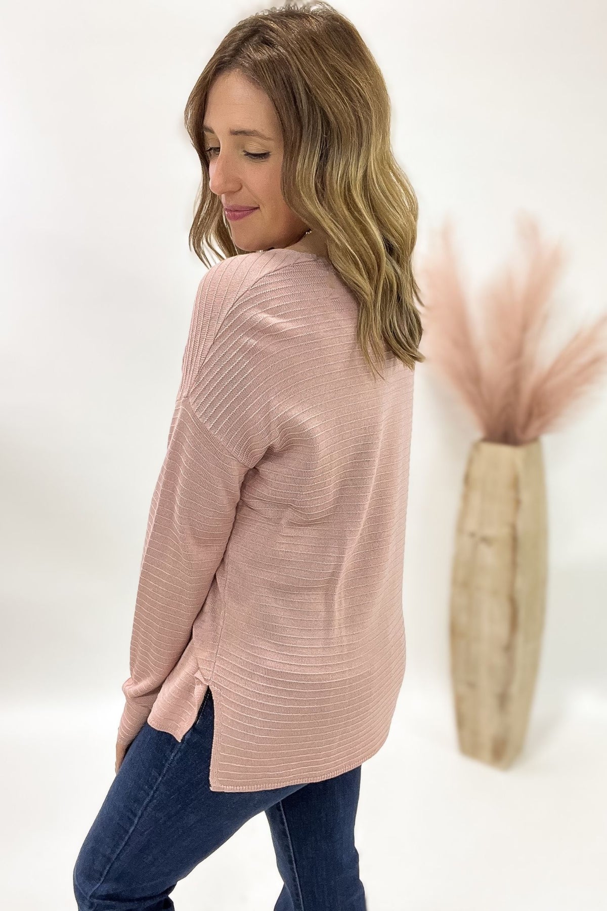 Woman wearing a pink sweater and blue jeans against a white background