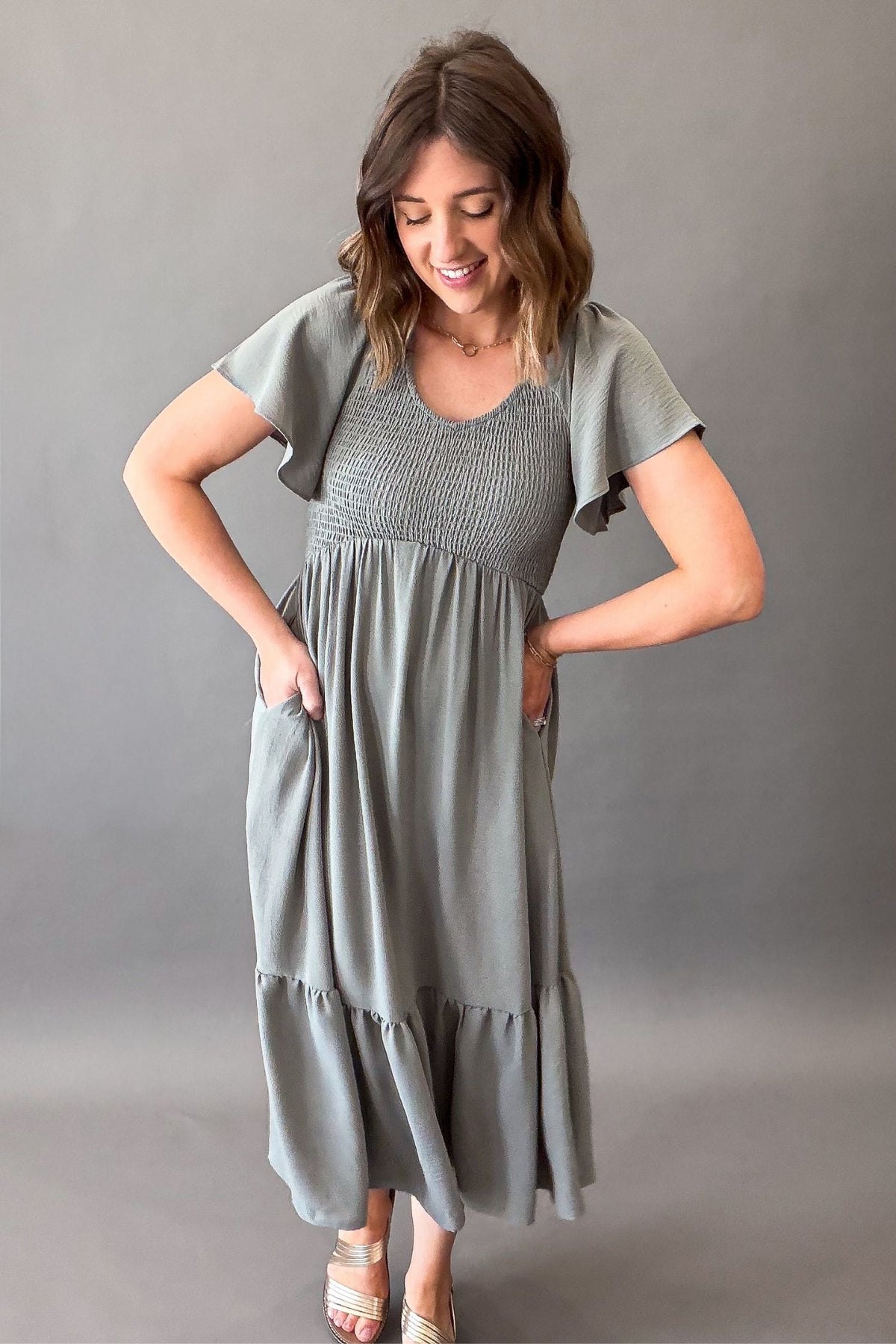 Woman wearing a dusty sage smocked midi dress showing side pockets