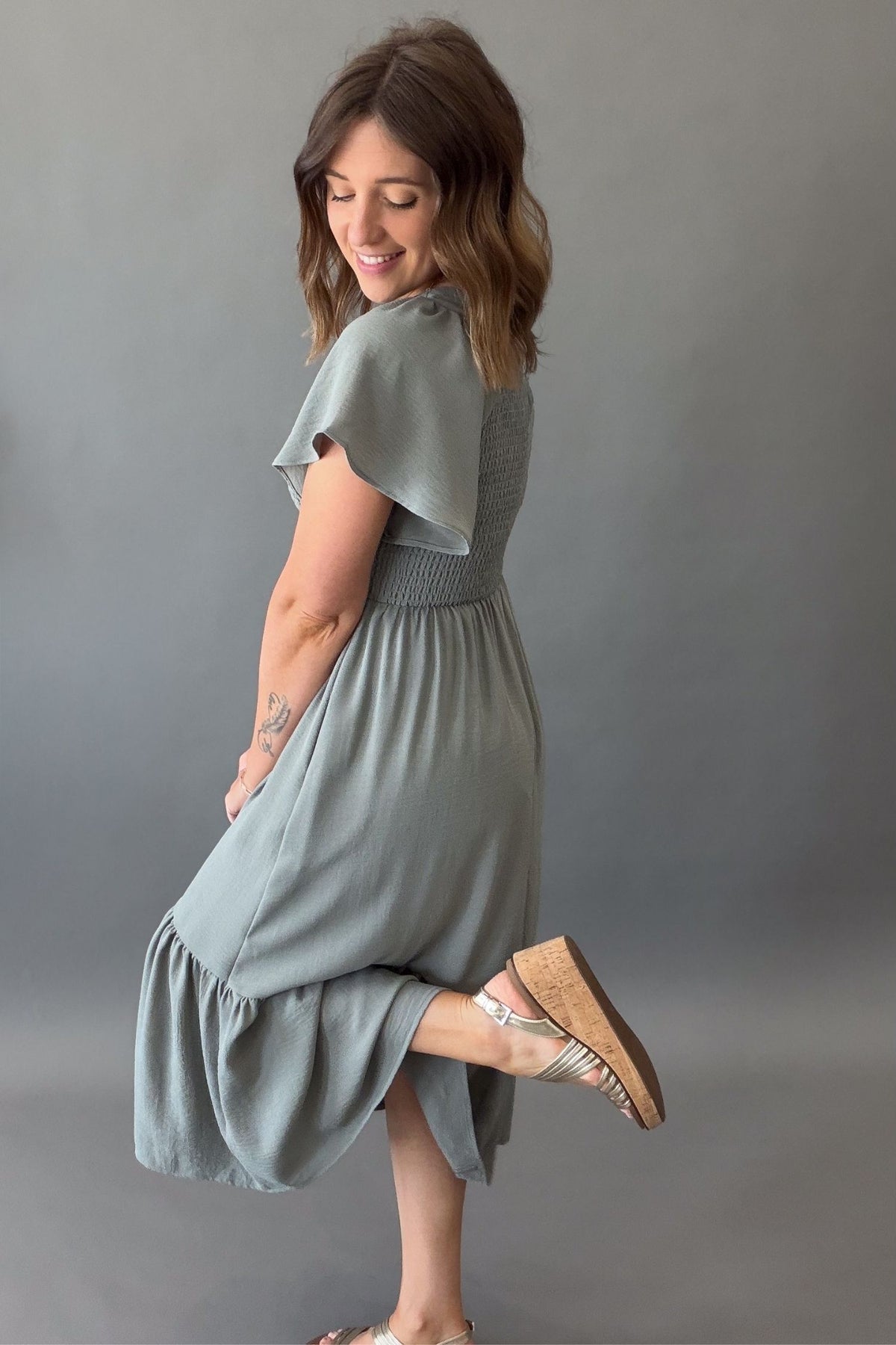 woman wearing a dusty sage midi dress showing flutter sleeve and back details