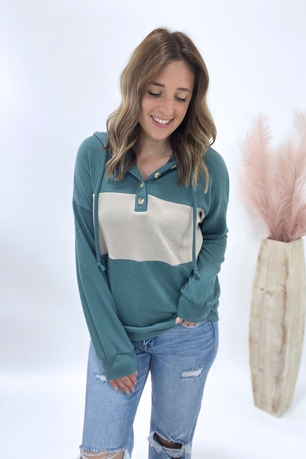 Woman wearing a teal and beige color-blocked shirt with ripped jeans on a white background