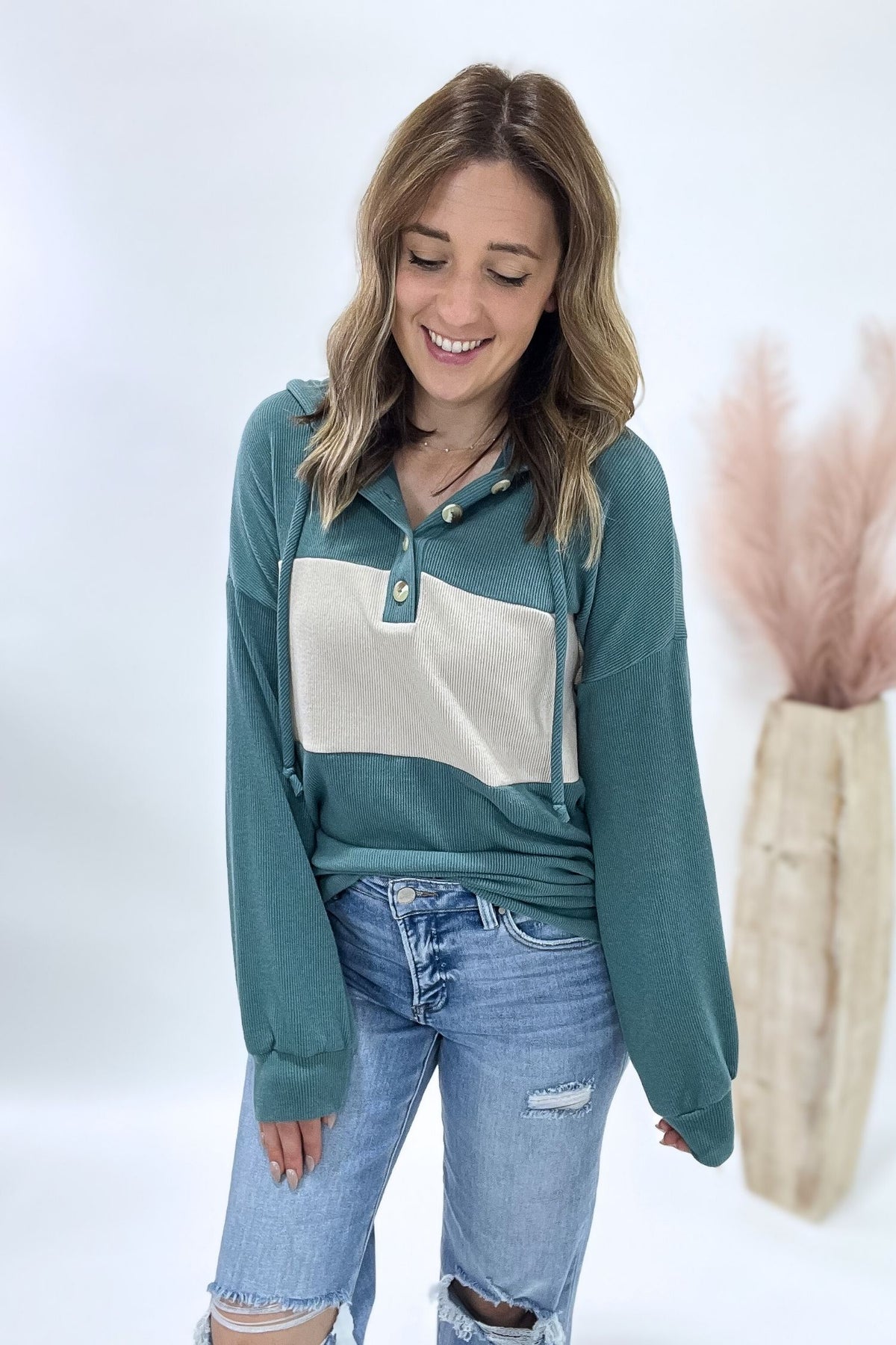 Woman wearing a teal and white long-sleeve shirt with blue jeans on a white background