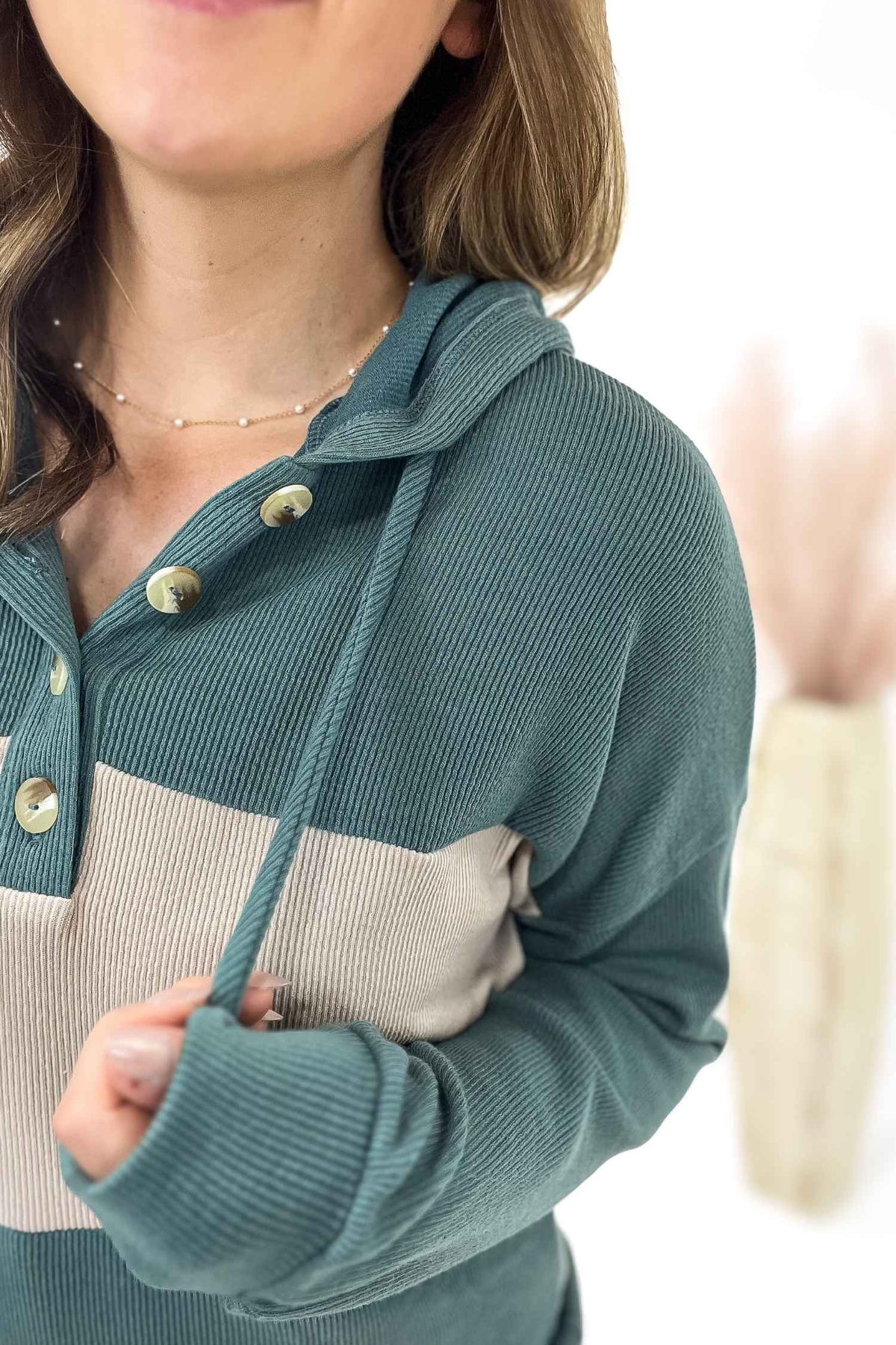 Person wearing a teal and beige long-sleeve top with button details on a blurred background