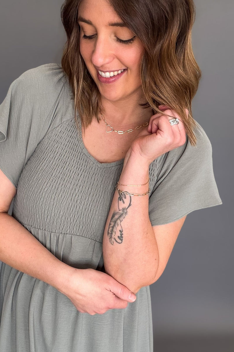 woman wearing a dusty sage smocked midi dress showing the smocked bust and flutter sleeve details