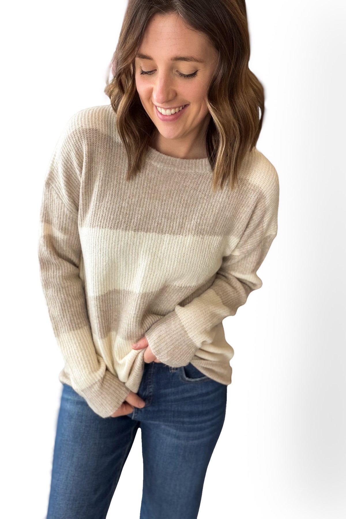 Woman wearing a beige sweater and blue jeans on a white background