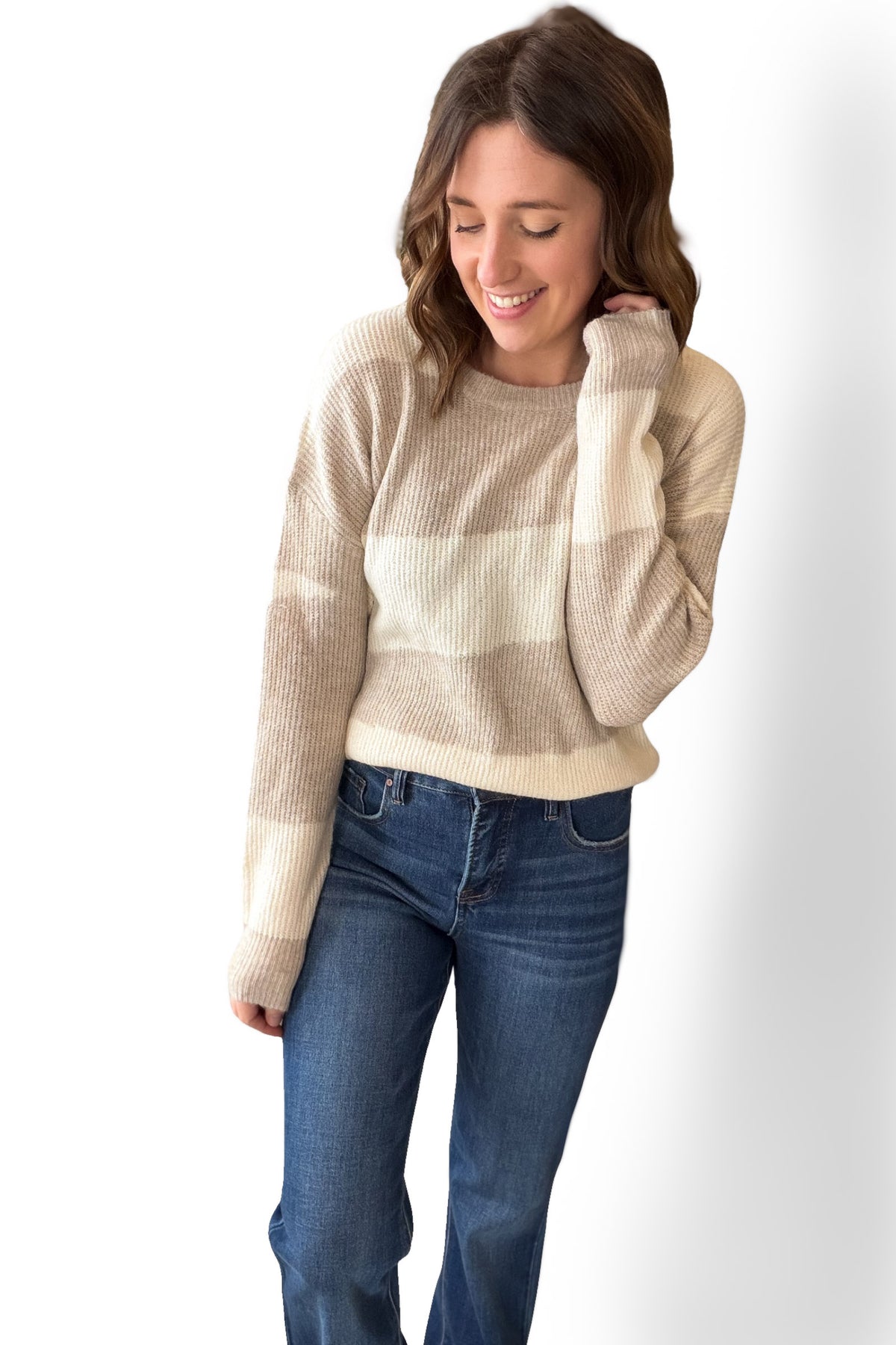 Woman wearing a beige and white striped sweater and blue jeans on a white background