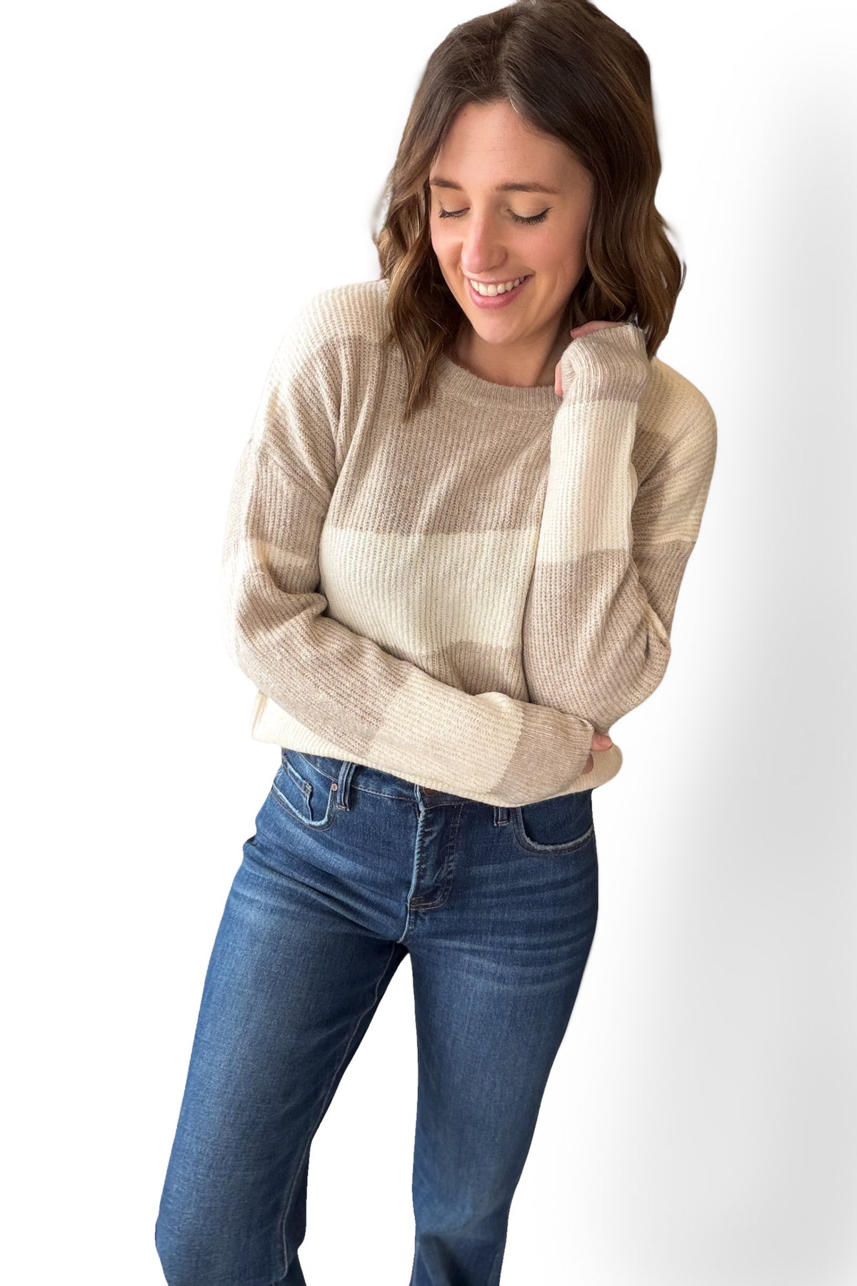 Woman wearing a beige sweater and blue jeans on a white background