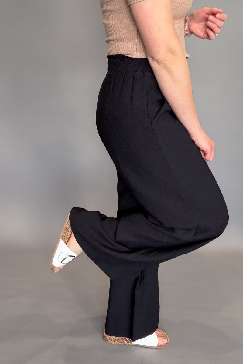 Person wearing black wide-leg pants on a gray background showing side details