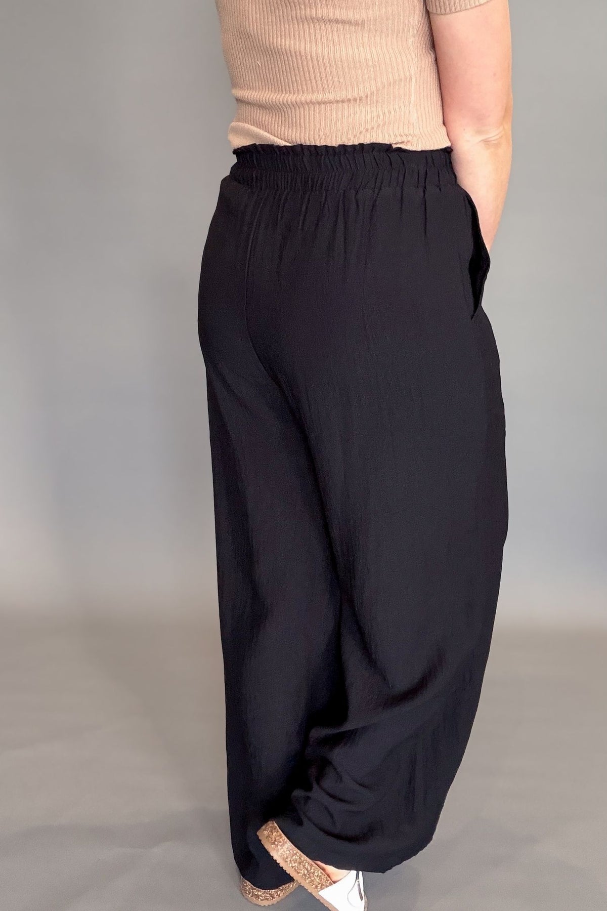 Person wearing black wide-leg pants and a beige top against a plain background showing back details