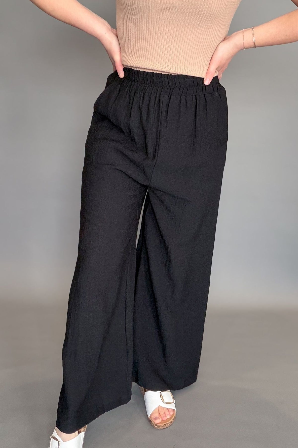 Person wearing black wide-leg pants and a beige top on a gray background