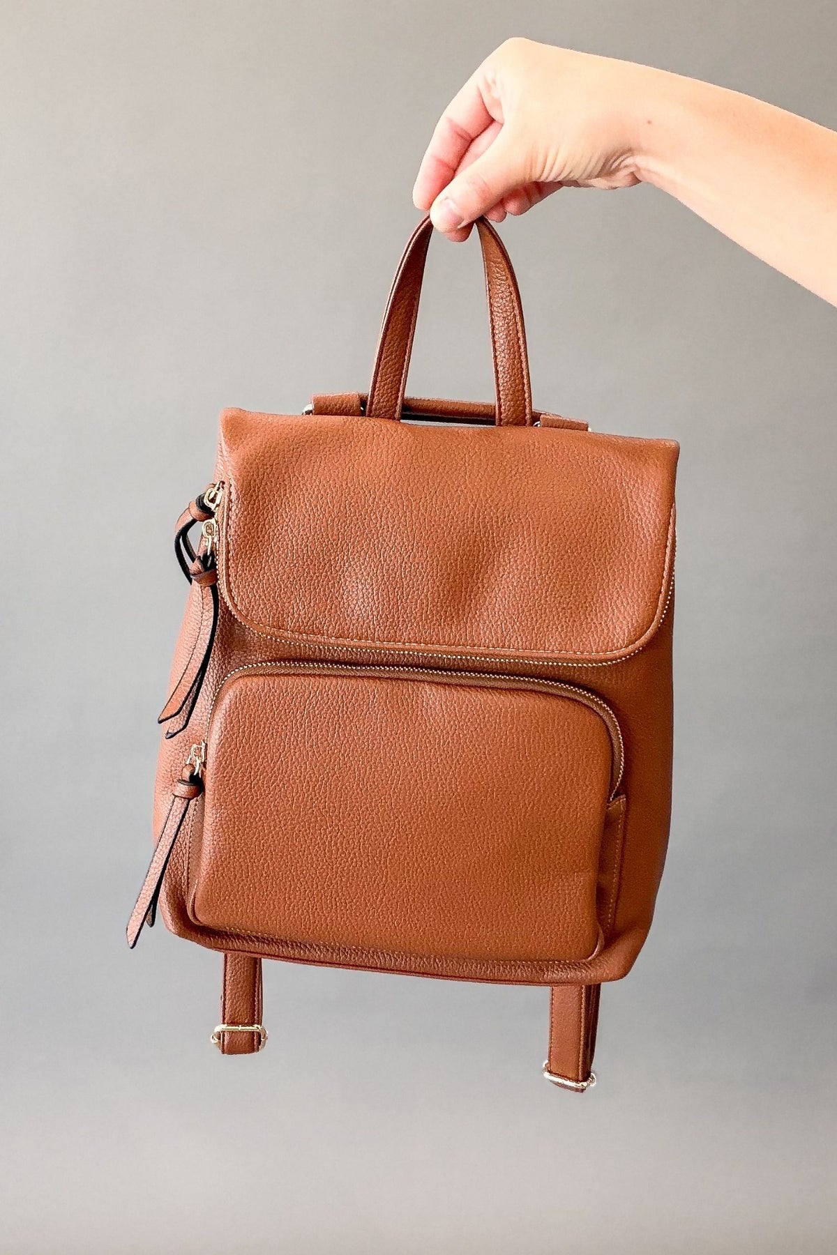 Woman holding a brown backpack with gold hardware showing a closed back and zipper details