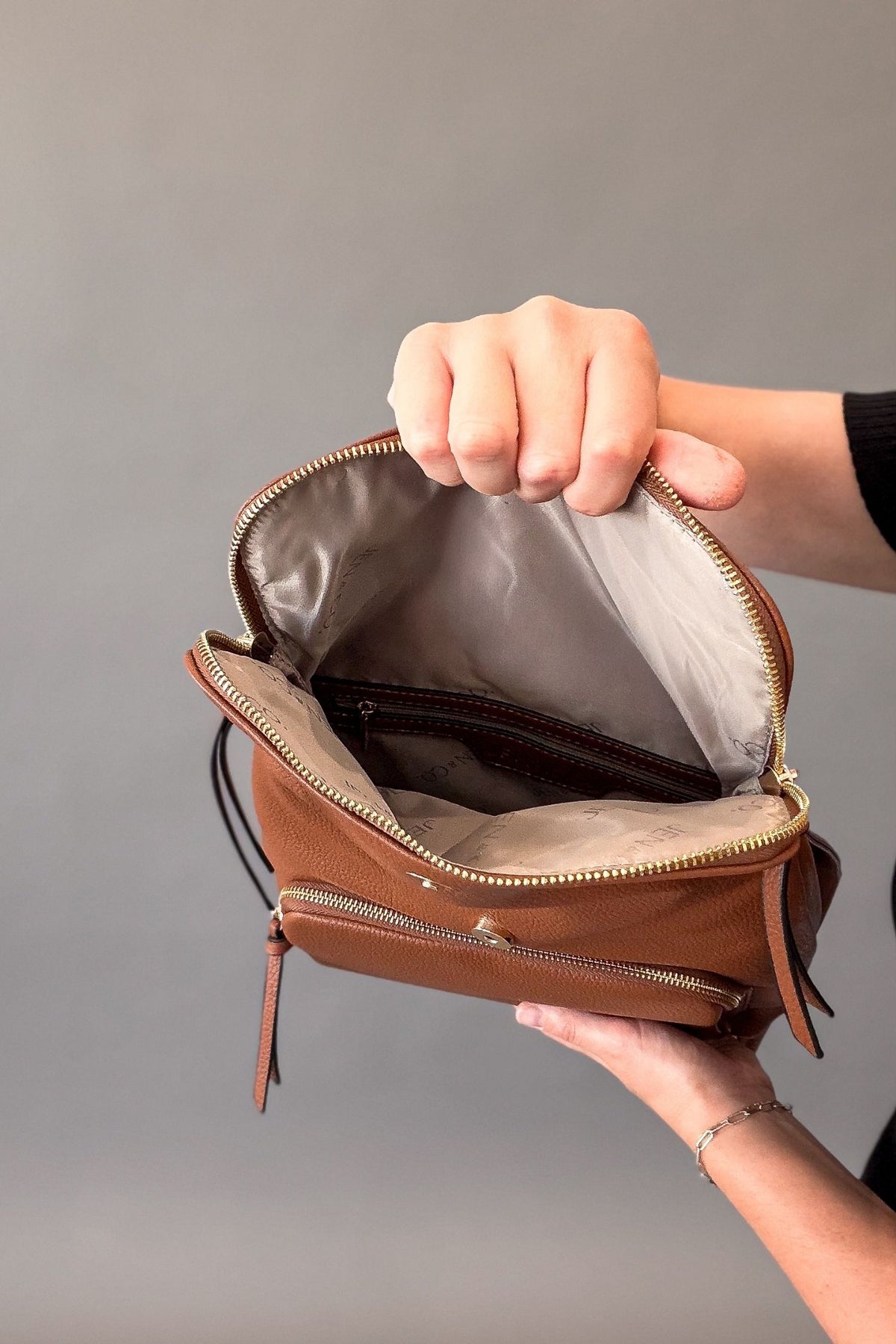 Woman holding the backpack open to show inside slip pockets and small inside zip pocket