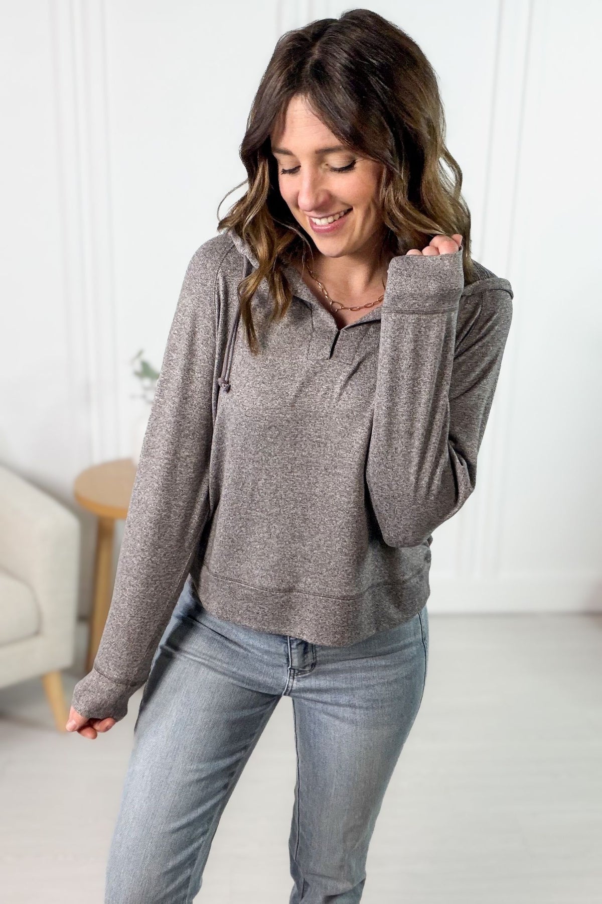 Woman wearing a mocha pullover and jeans in a room with white walls and a light-colored floor.