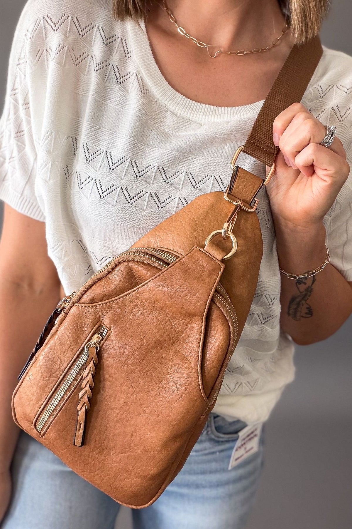 Woman wearing a caramel sling crossbody bag with a white top and blue jeans