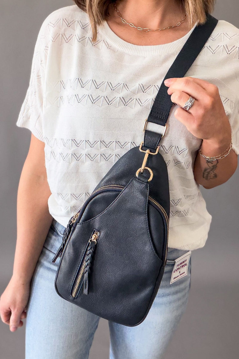 woman wearing a navy crossbody bag with a white top and blue jeans on a grey background