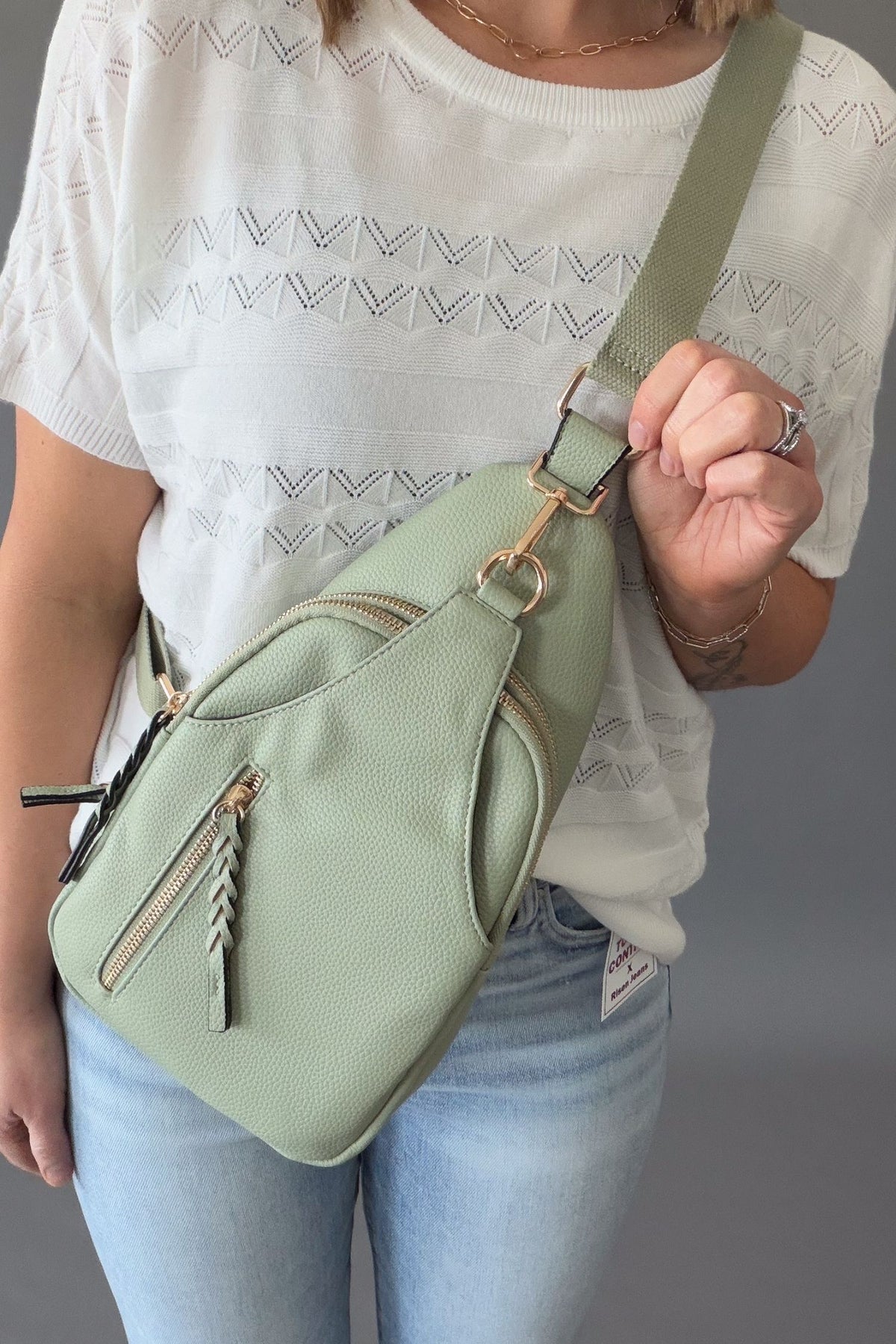 woman wearing a light sage crossbody with a white top and blue jeans
