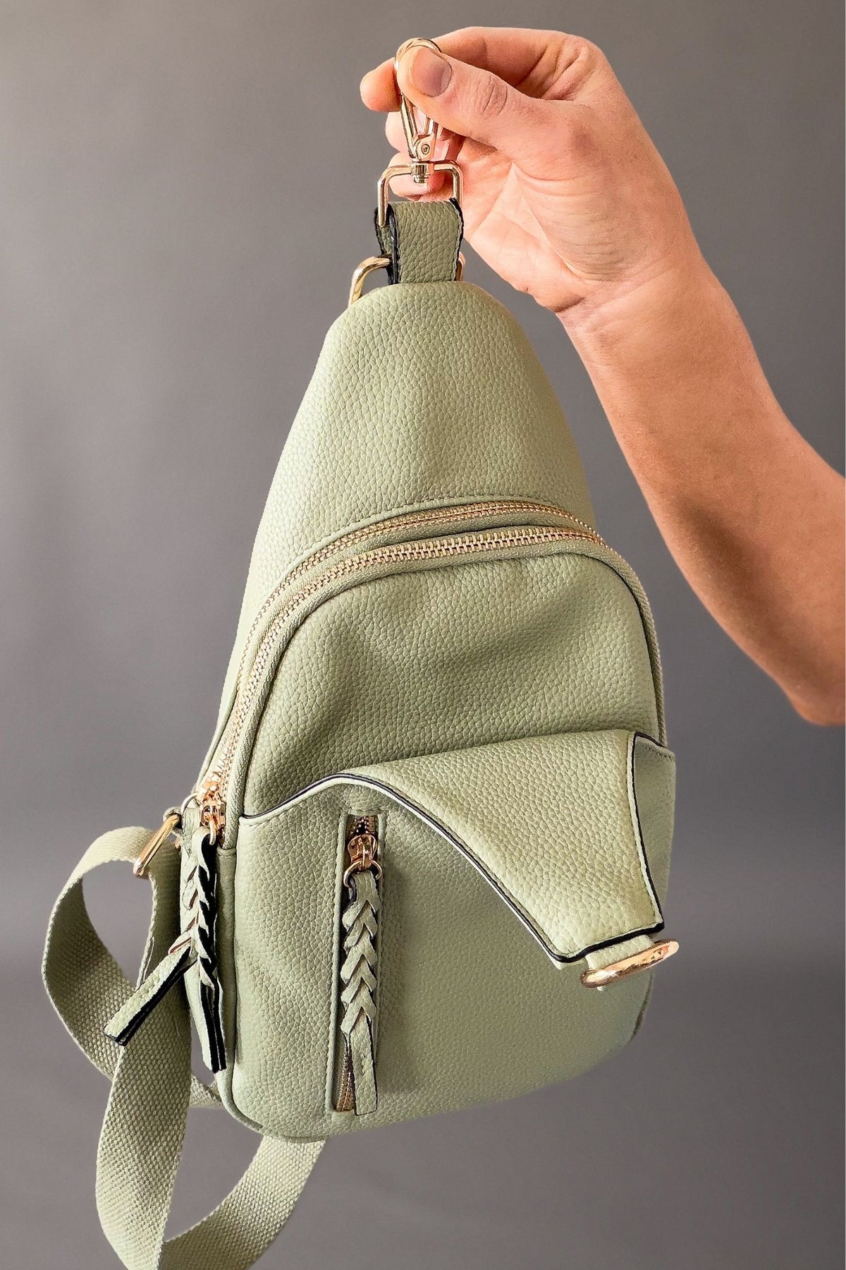 woman showing a light sage crossbody with the strap open to show front pocket 