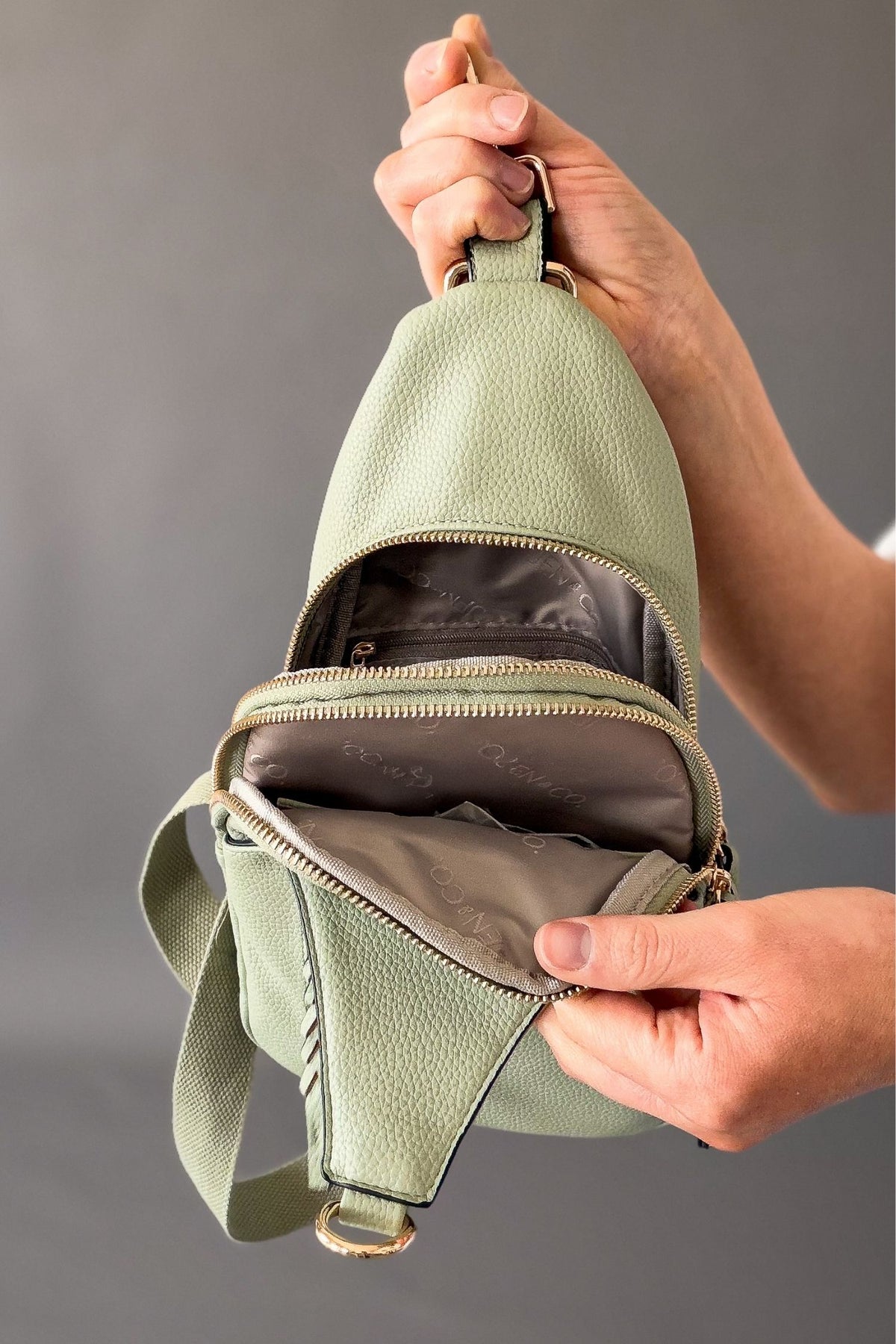 woman holding sling bag and showing 2 zipper compartments on the sling bag
