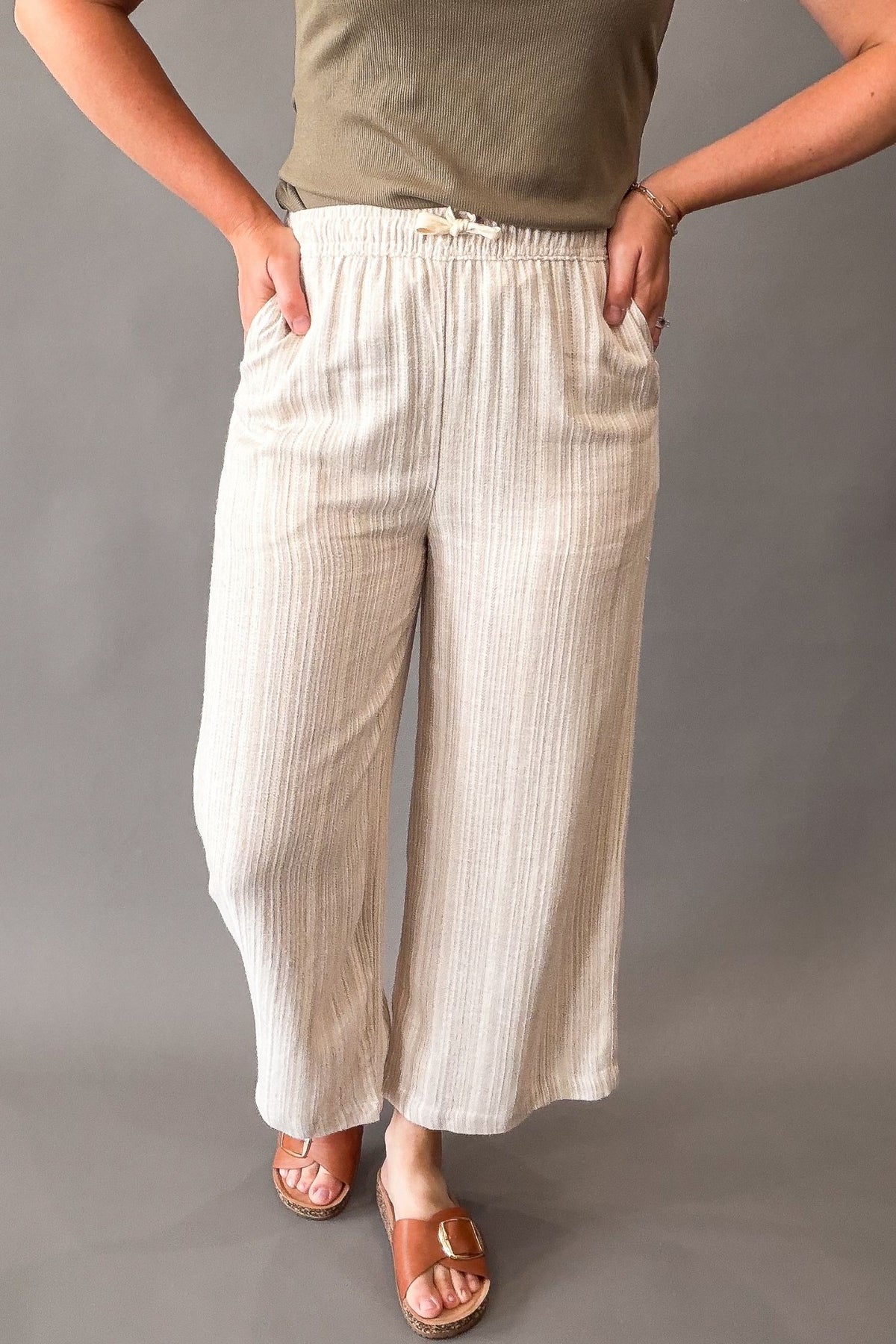 A person wearing loose, wide-leg cropped pants in a light cream or off-white woven fabric with subtle vertical texture. The pants have an elastic waistband with a small white drawstring and side pockets.