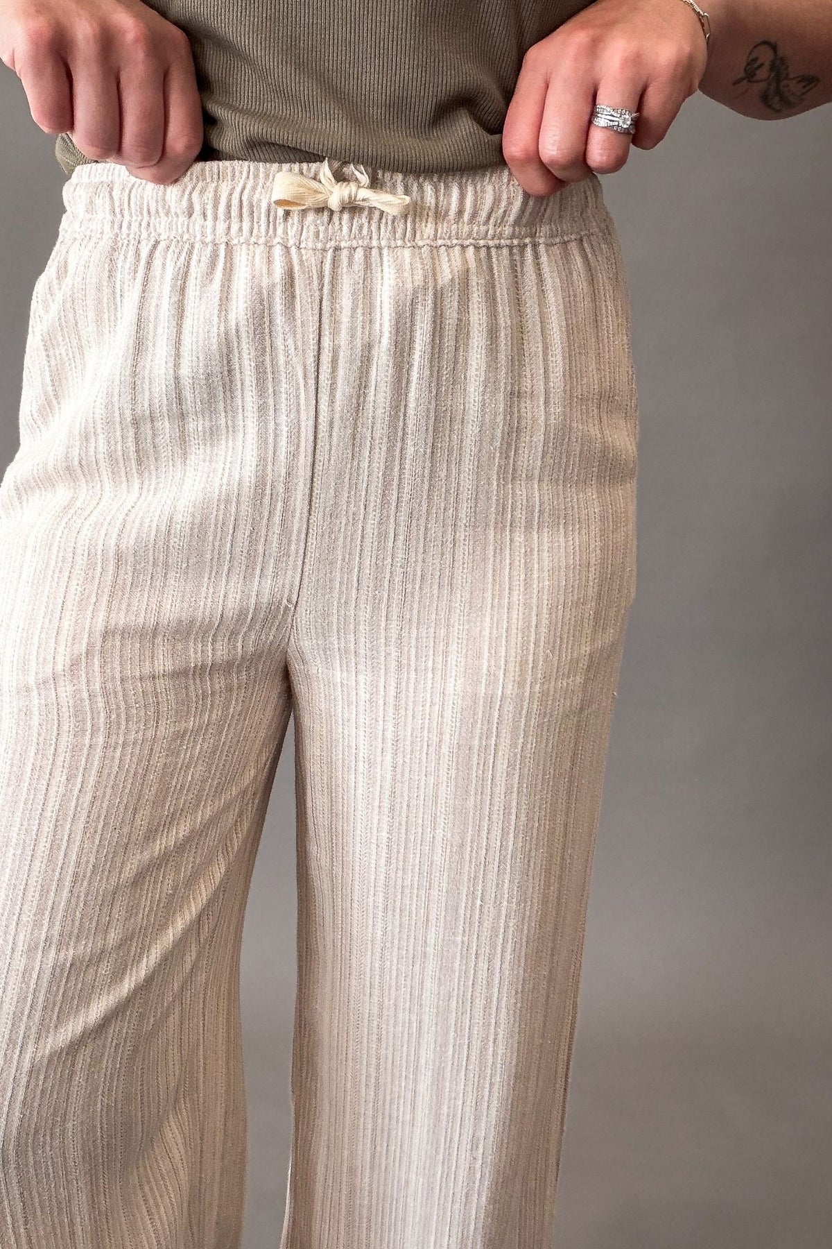 Beige textured wide-leg pants with an elastic waistband and a small fabric bow detail, shown on a model.