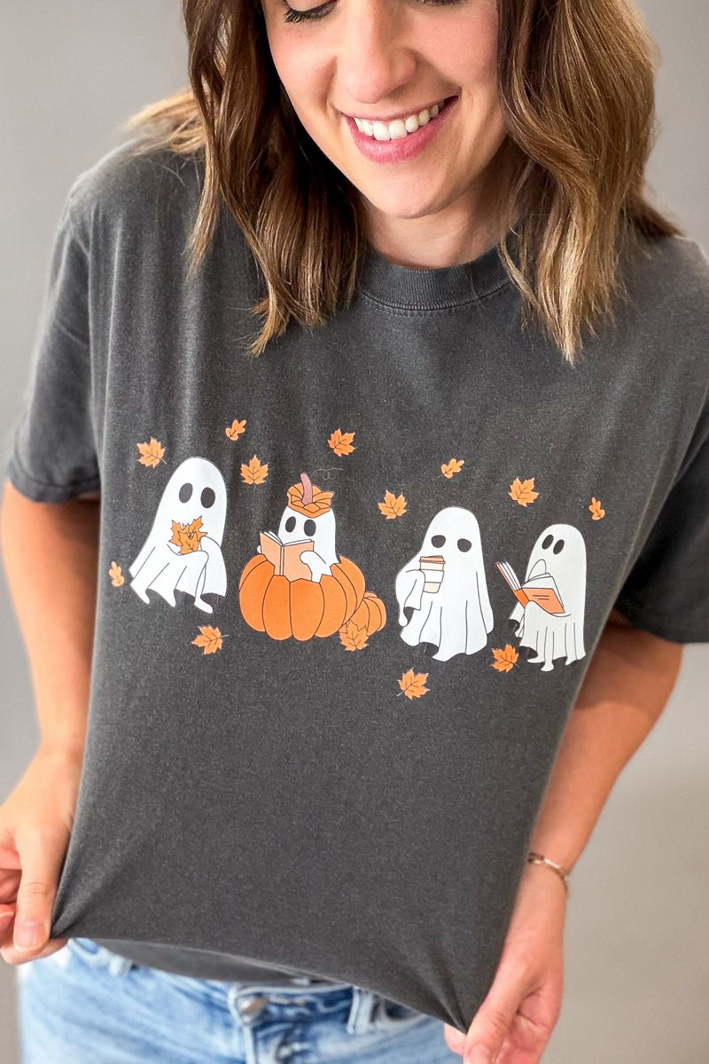 A woman wearing a dark gray graphic t-shirt with a design of ghosts, pumpkins, and orange leaves, paired with blue jeans.